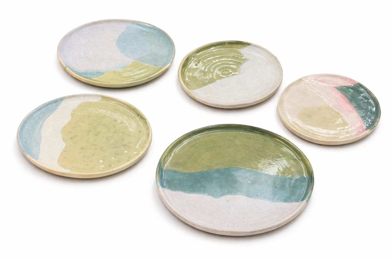 Cinq petites assiettes en céramique colorées avec un motif abstrat en pastel, disposées sur un fond blanc.