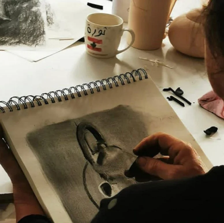 Une personne en train de dessiner un portrait d'une personne avec des crayons dans un carnet spiralé, vu de près.