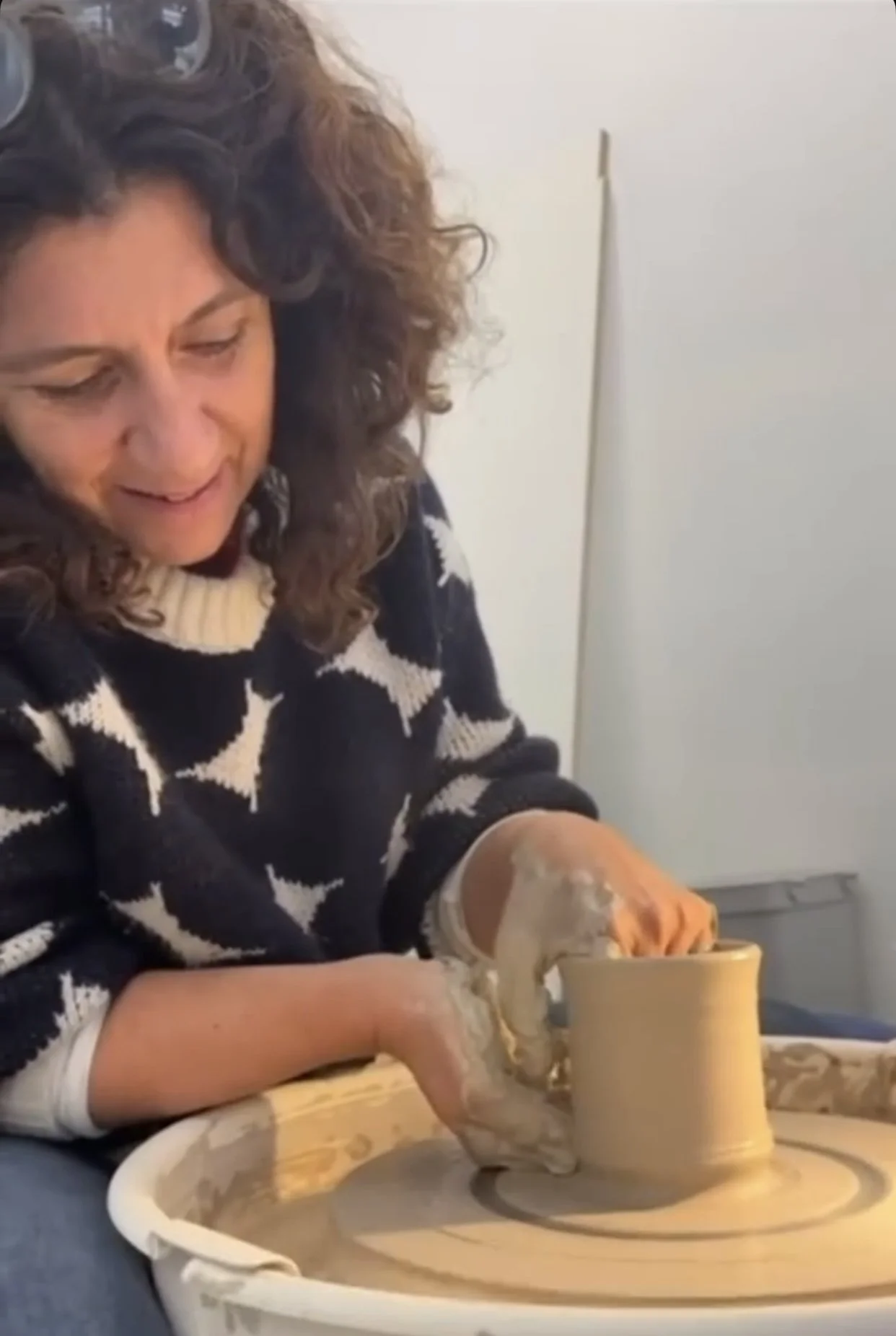 Une femme fait de la poterie sur un tour de potier, concentrée sur la création d'un vase en argile.