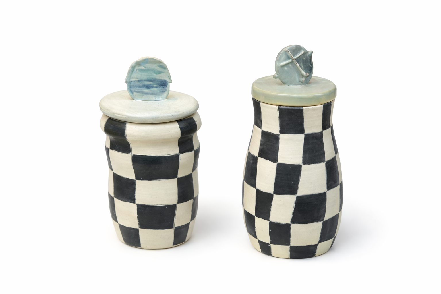 Deux boîtes en céramique avec motif de damier noir et blanc, couvercles avec de petites sculptures en forme de pierres ou de cylindres.