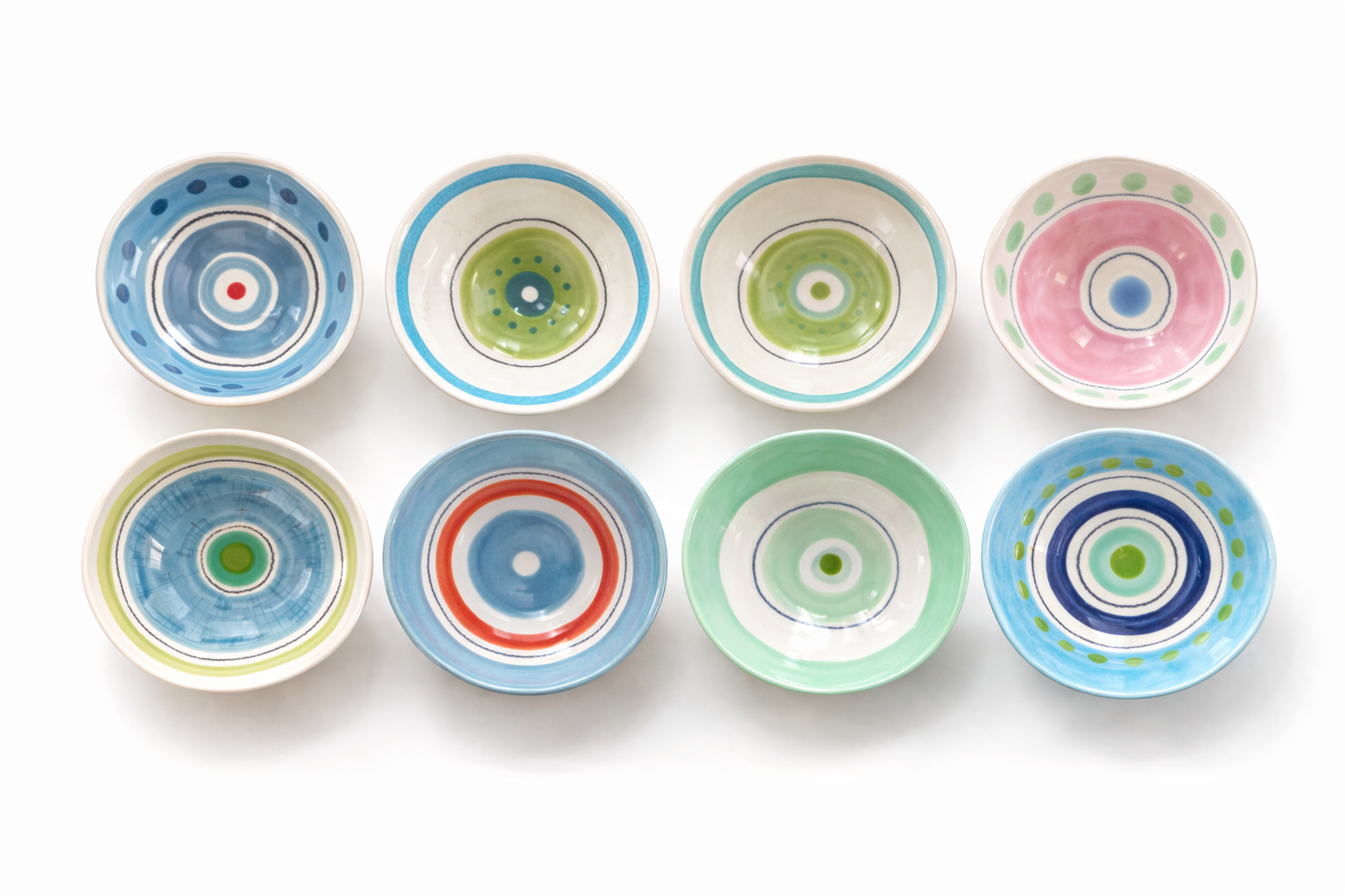 Neuf petites assiettes en céramique colorées avec des motifs circulaires, disposées en deux rangées sur un fond blanc.