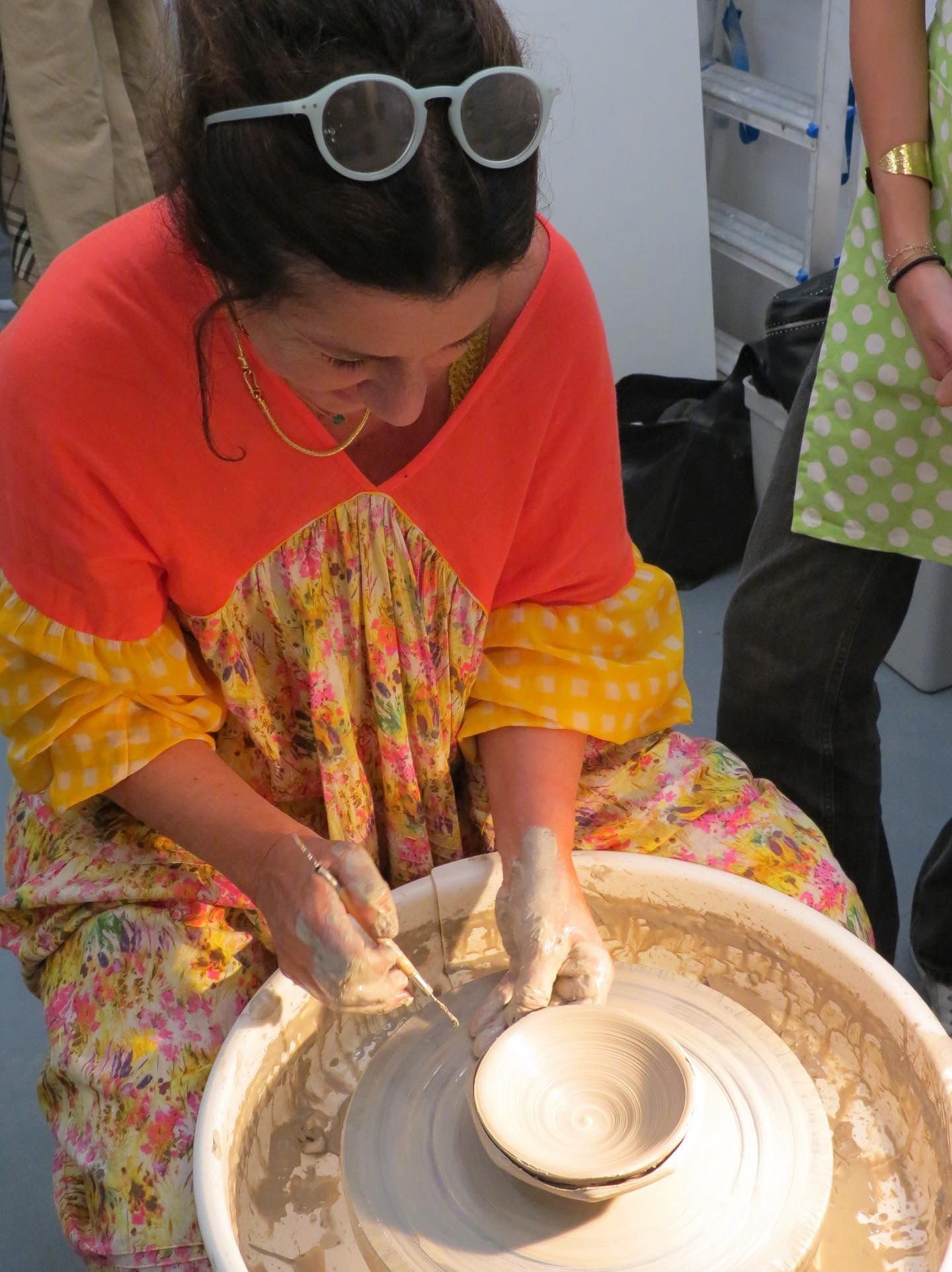 Une personne travaille pour faire tourner un gobelet de céramique sur un tour de potier. Il y a de la pâte à modeler autour du tour, et deux éponges visibles à côté.