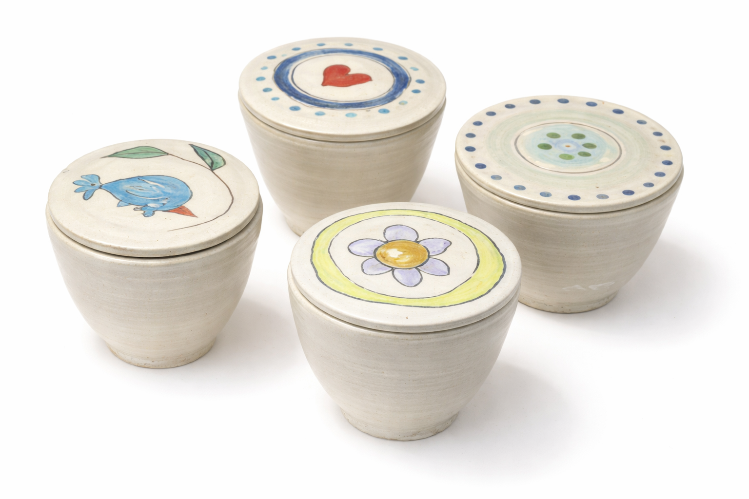Cinq petites boîtes en céramique avec des couvercles décorés de dessins colorés, représentant un cœur, un oiseau, une fleur, et des motifs abstraits, disposées sur un fond blanc.