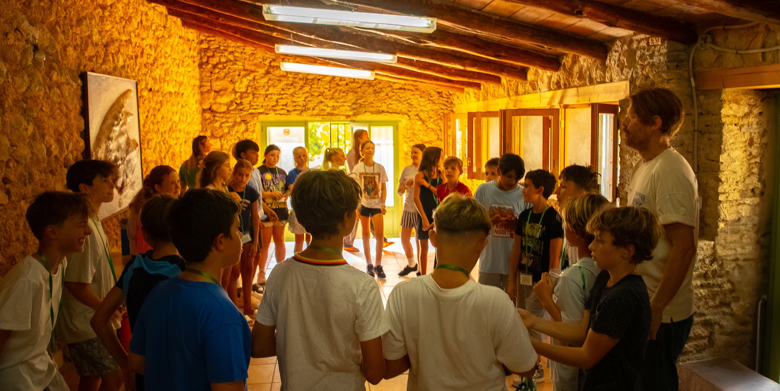 Group of friends sitting on the beach, one playing guitar, others holding drinks, during sunset.