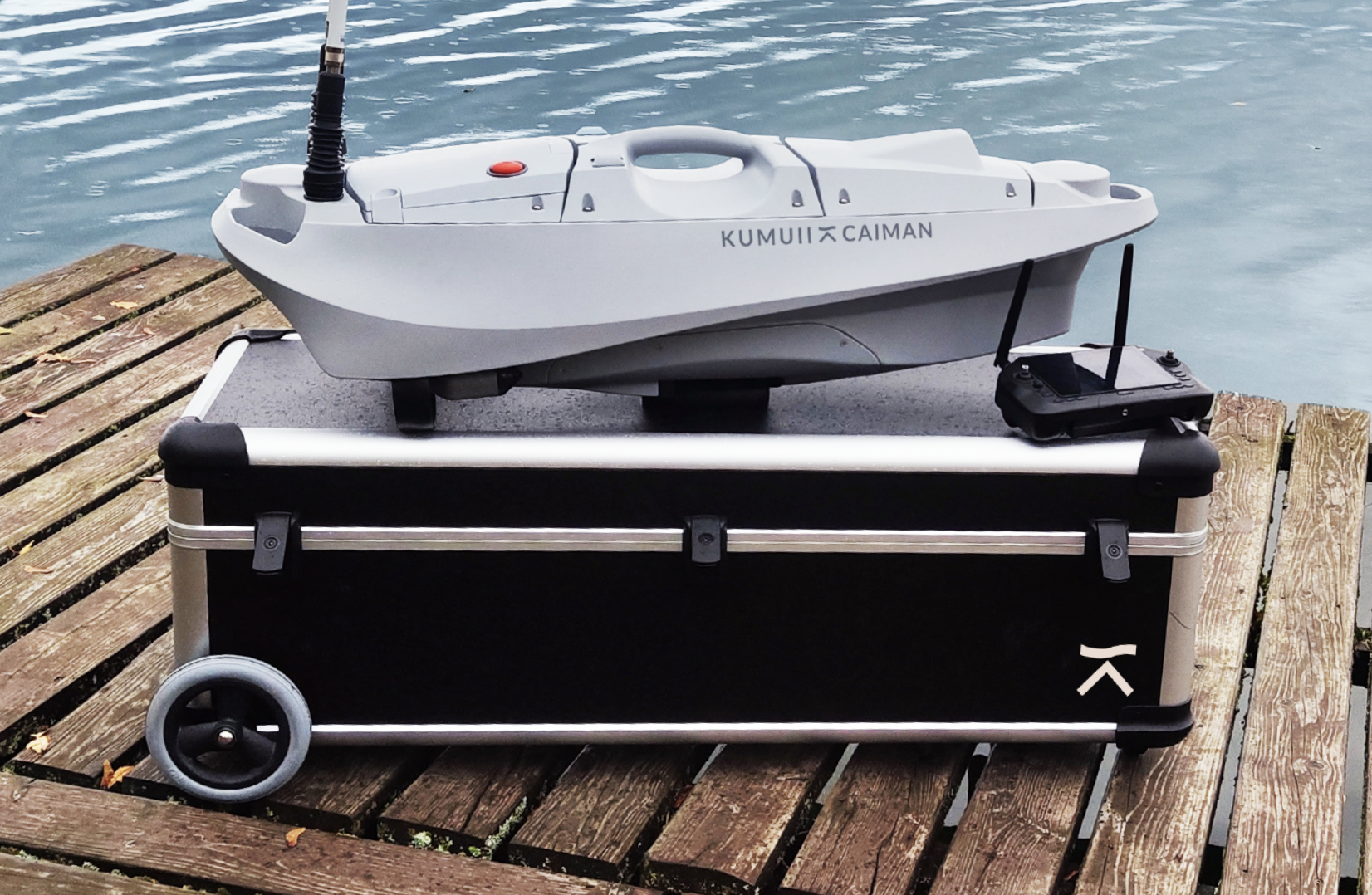 Ein ferngesteuertes Boot auf einem schwarzen Transportkoffer am Steg im Wasser.