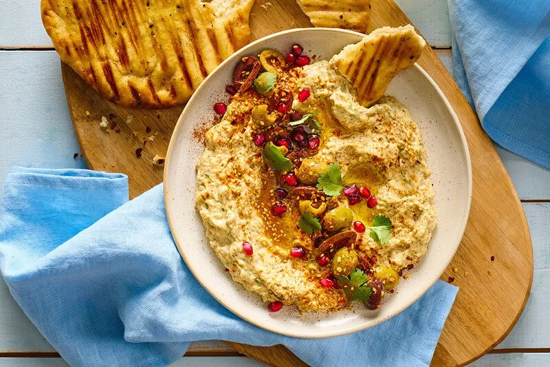 Zelfgemaakte baba ganoush in een kom gegarneerd met granaatappelpitjes, olijven, koriander en chilivlokken, geserveerd met gegrild platbrood
