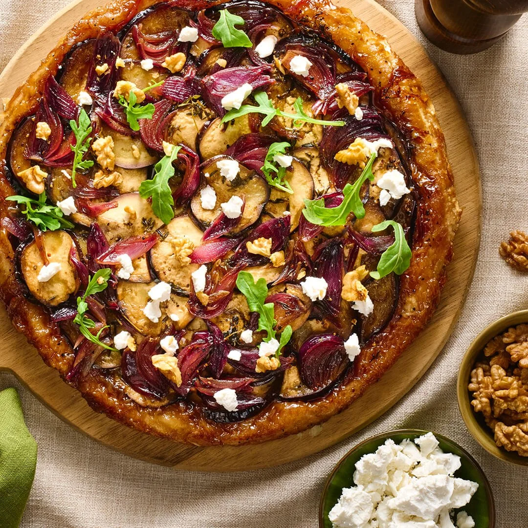 plank met daarop een tarte tatin van aubergine en rode ui gegarneerd met rucola geitenkaas en walnoten