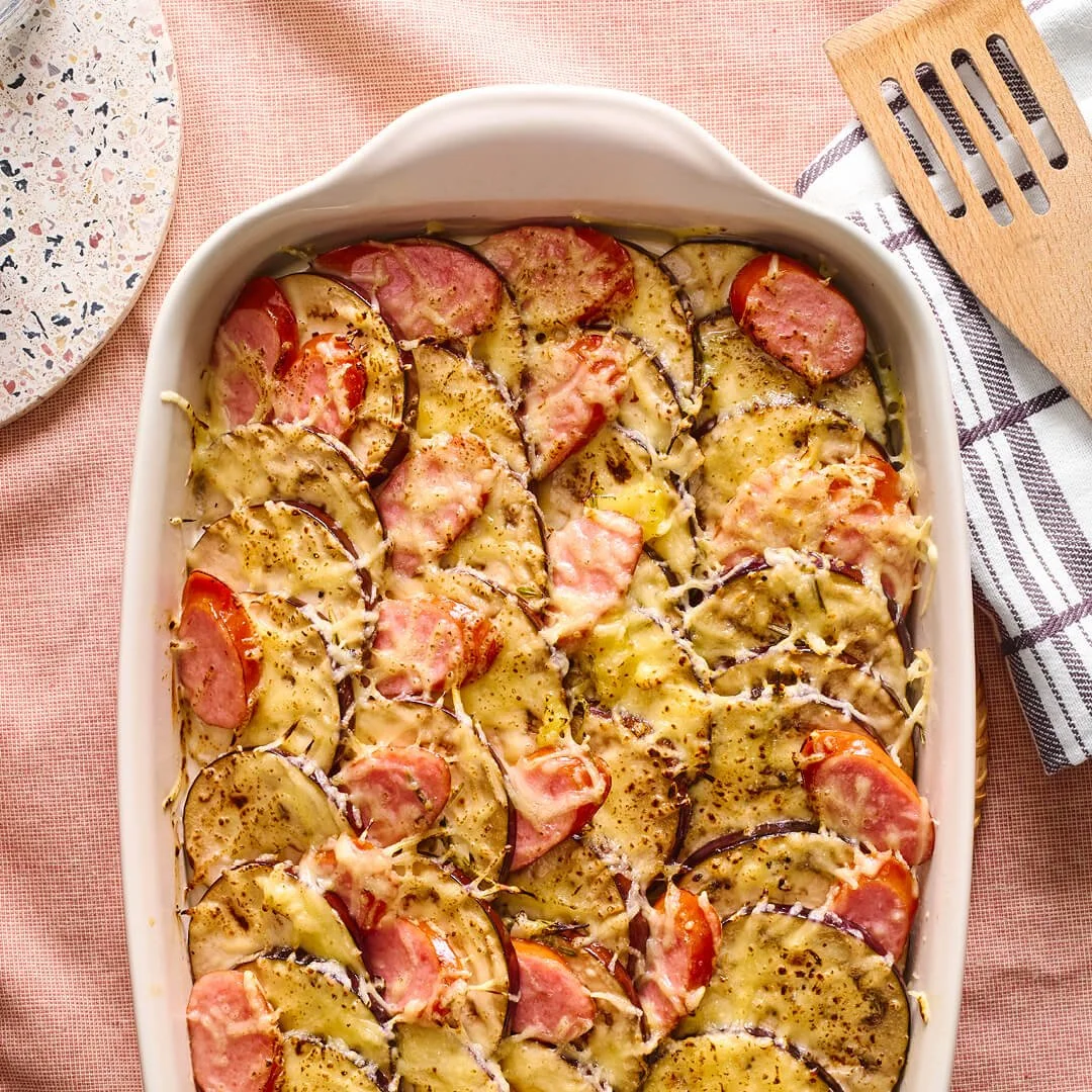 gratin van aubergine in een witte ovenschaal met rookworst aardappel en oude kaas