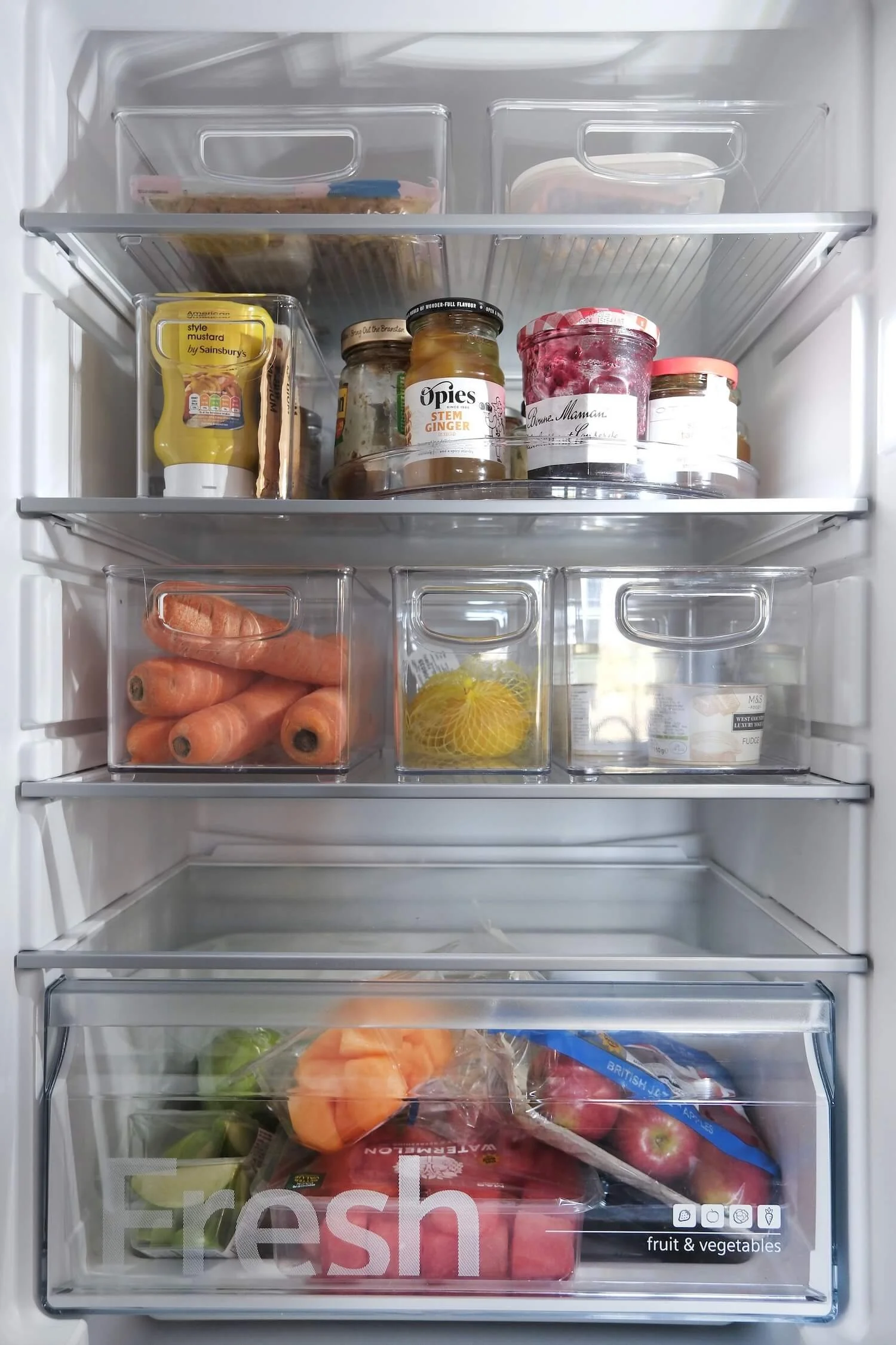 A fridge neatly organised using transparent storage containers and bespoke labels. 