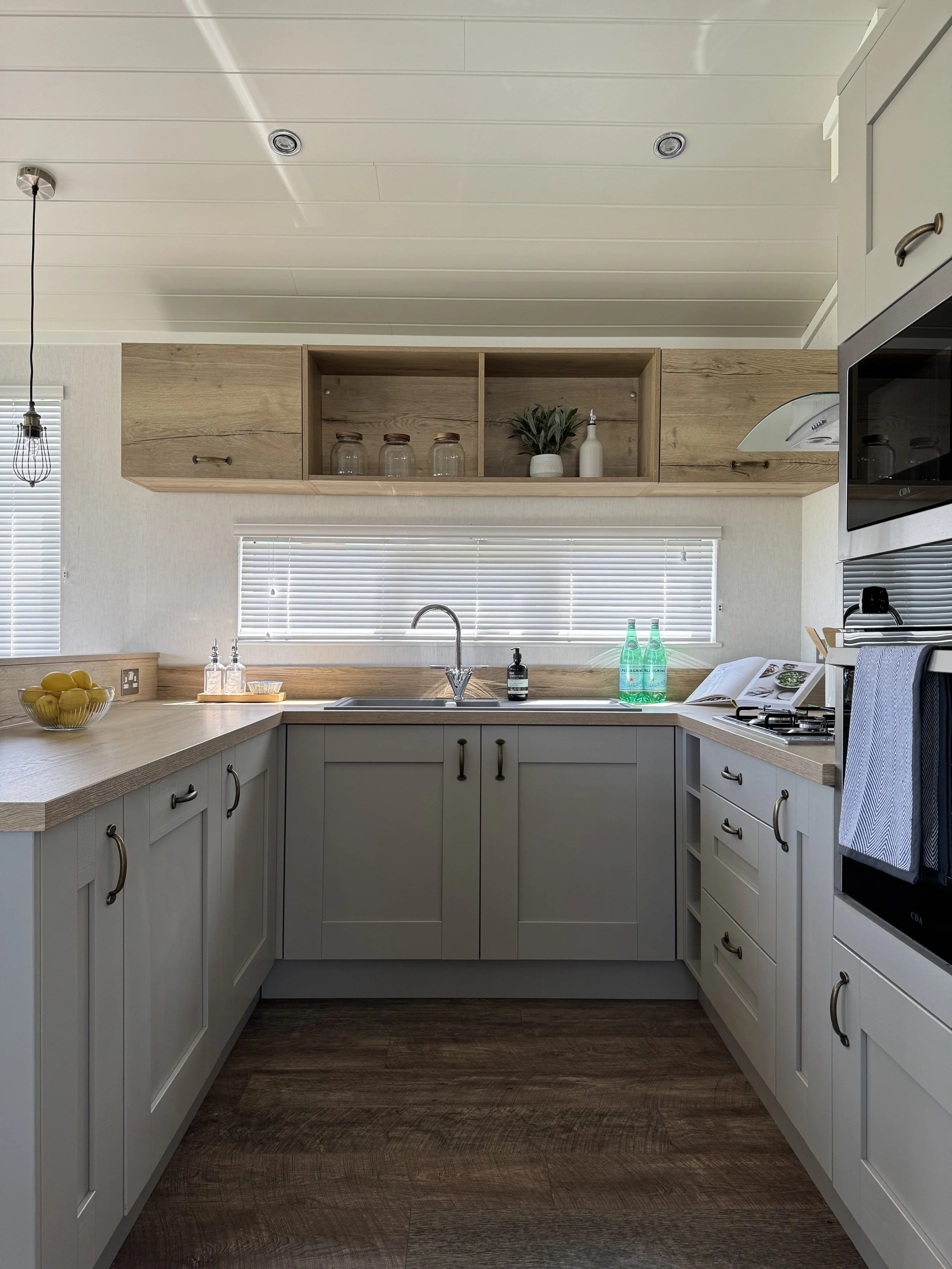 A modern, bright kitchen with white cabinets, a large island with a countertop, and large glass doors leading to an outdoor patio with greenery. The kitchen is well-lit with sunlight streaming in.