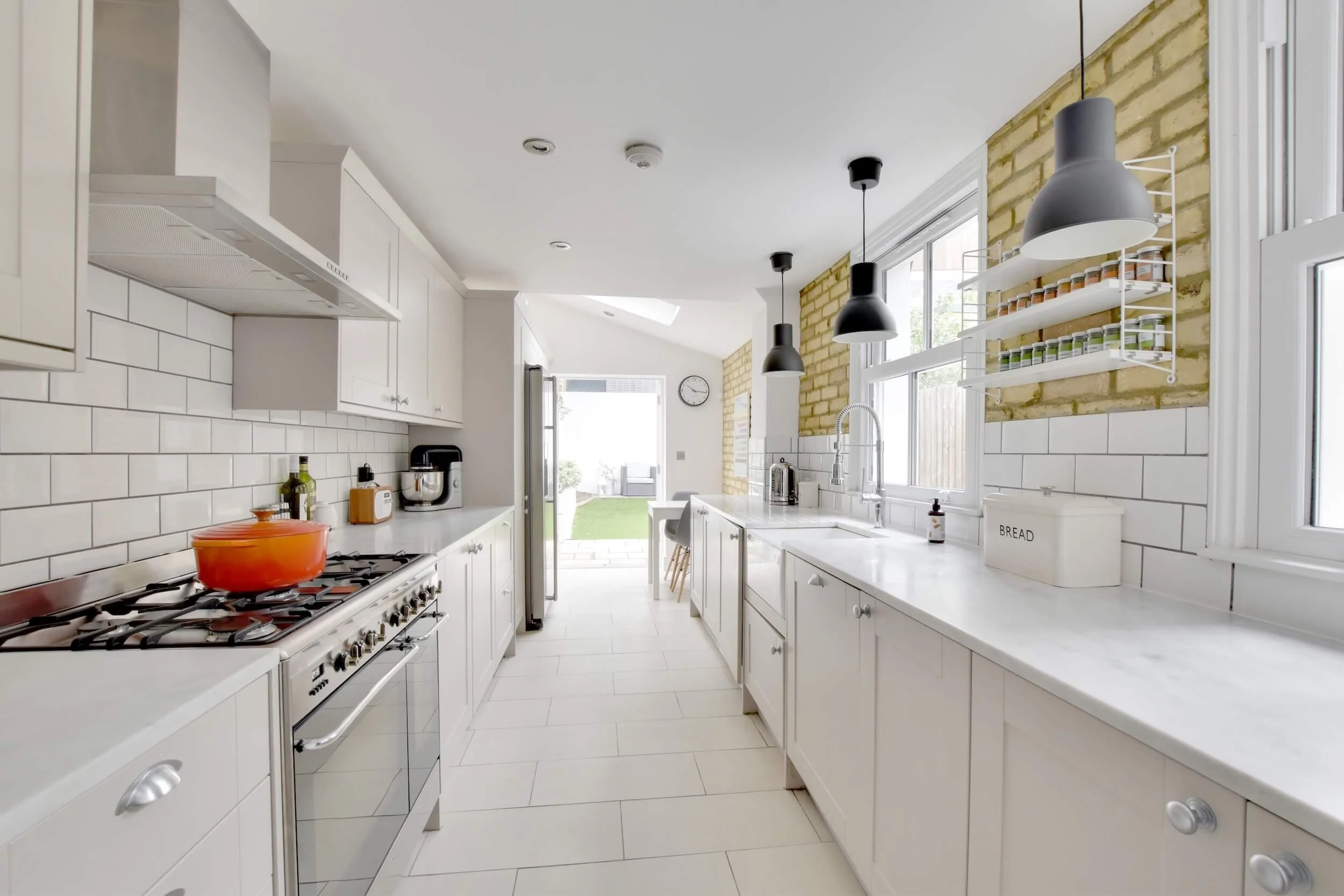 Bright modern kitchen with white cabinets, white backsplash, black pendant lights overlooking backyard.
