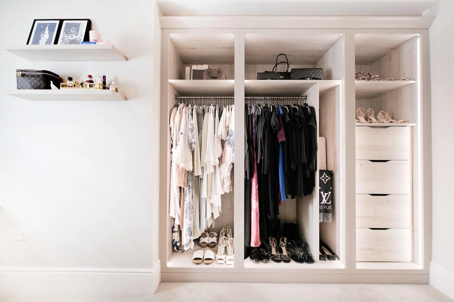 A neatly organised closet in a dressing room, showing clothes hung up in order of colour and shoes and scarfs neatly arranged. 