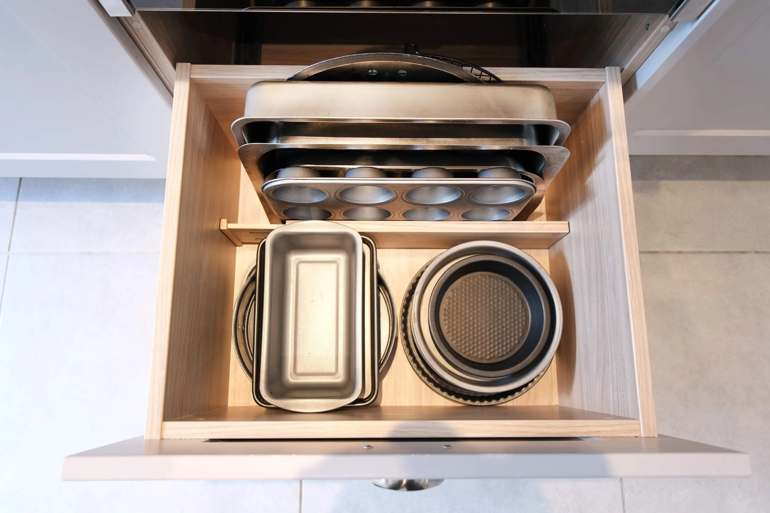Open kitchen drawer containing baking pans, baking sheets, and cake pans stacked neatly.