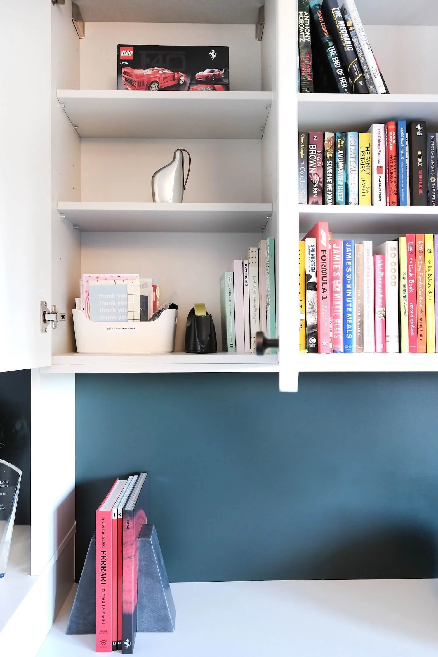 A tidy cupboard in an office, showing books neatly arranged and a stack of greeting cards in a storage container with bespoke label. 