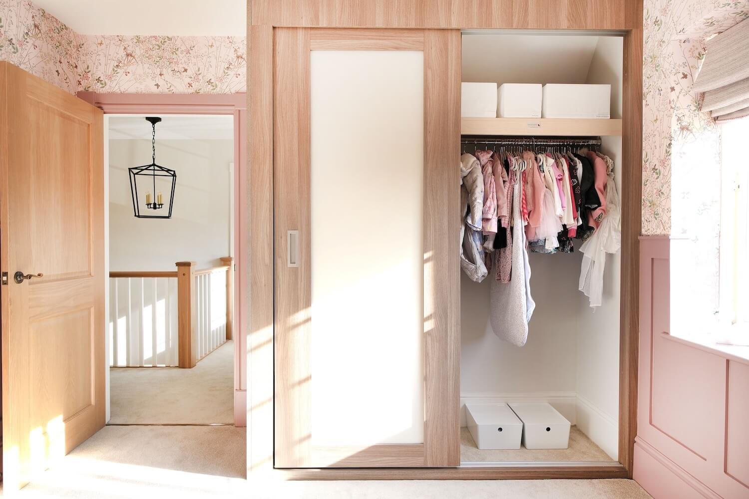 An organised wardrobe in a baby's room, with hanging clothes and storage boxes and containers with bespoke labels. 