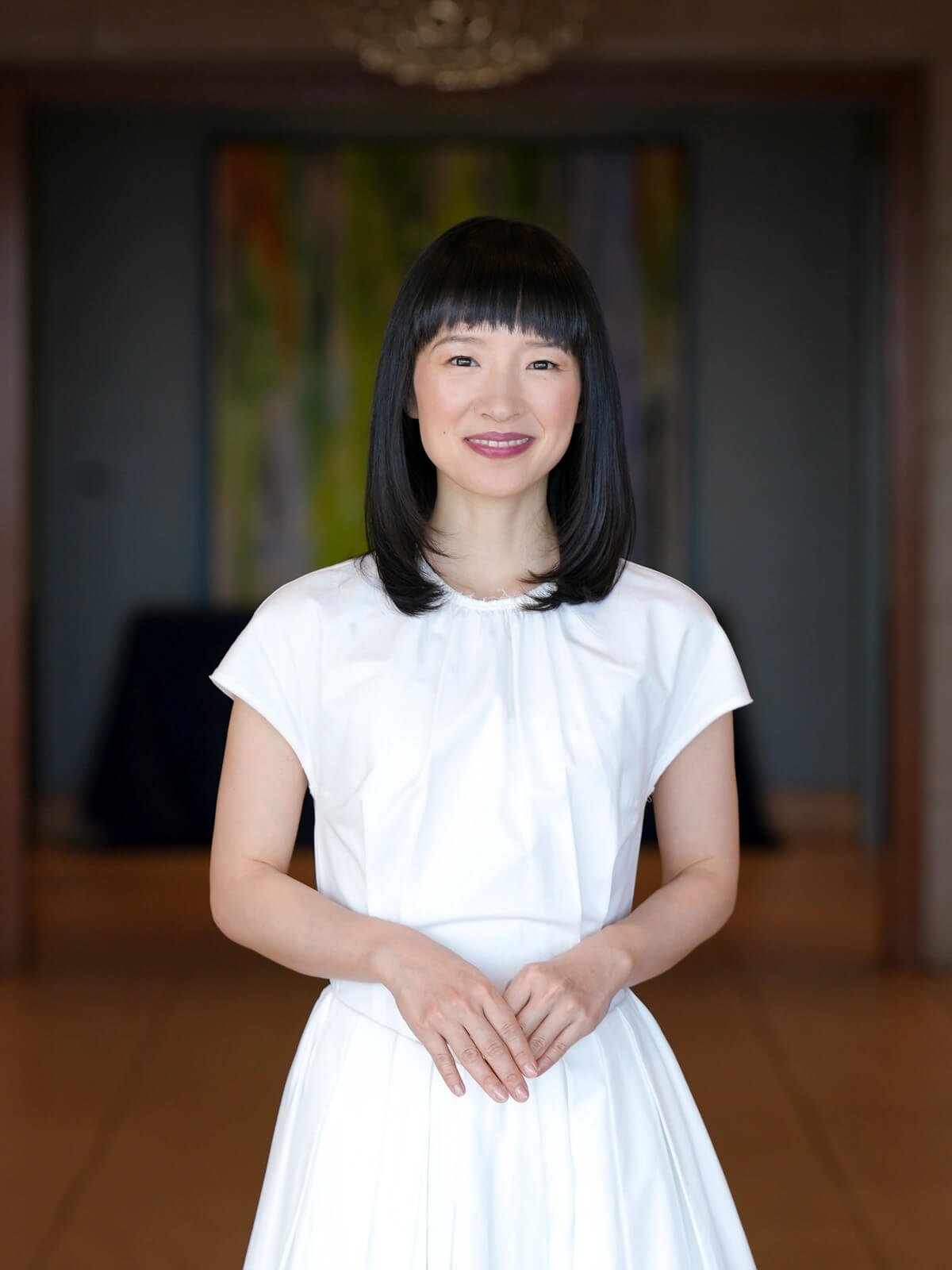 Marie Kondo smiling wearing a white dress and hands folded together.