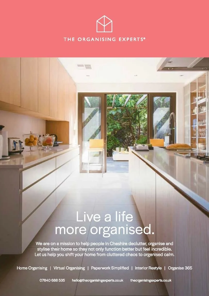 A modern, bright kitchen with white cabinets, a large island with a countertop, and large glass doors leading to an outdoor patio with greenery. The kitchen is well-lit with sunlight streaming in.