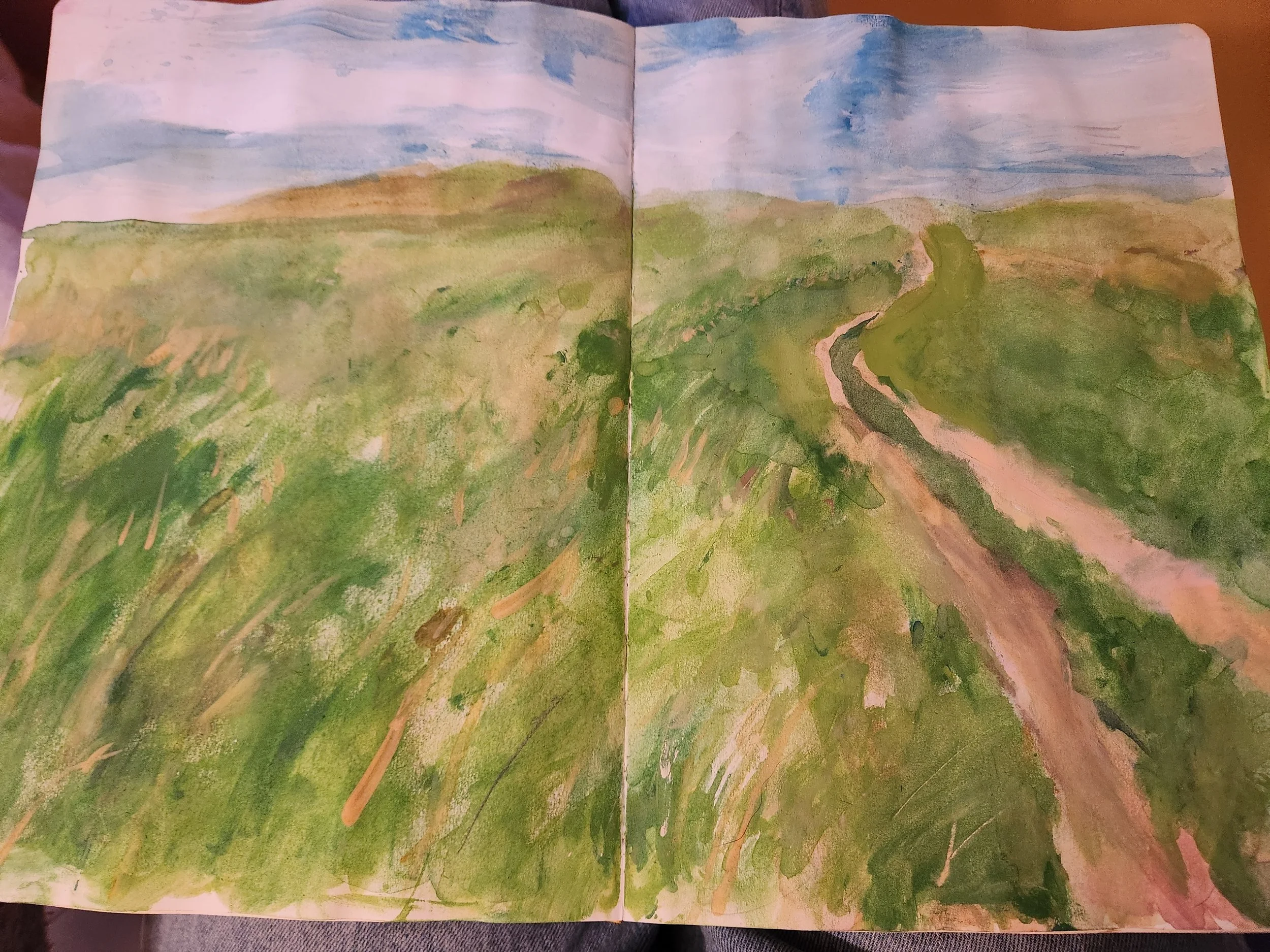 A watercolor painting of a countryside landscape with a dirt road winding through green fields and rolling hills under a cloudy sky.