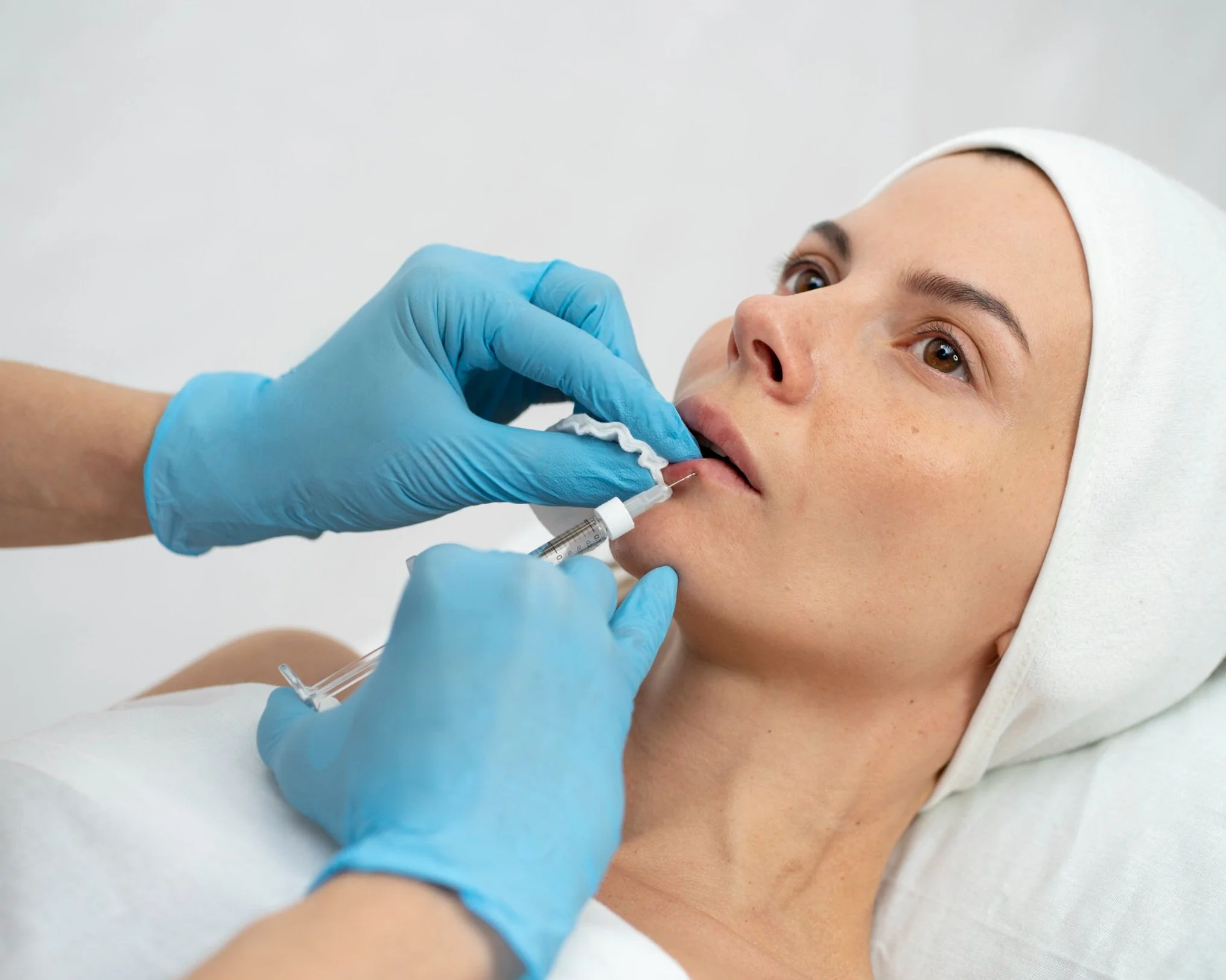 Gloved hands injecting filling into woman's lip