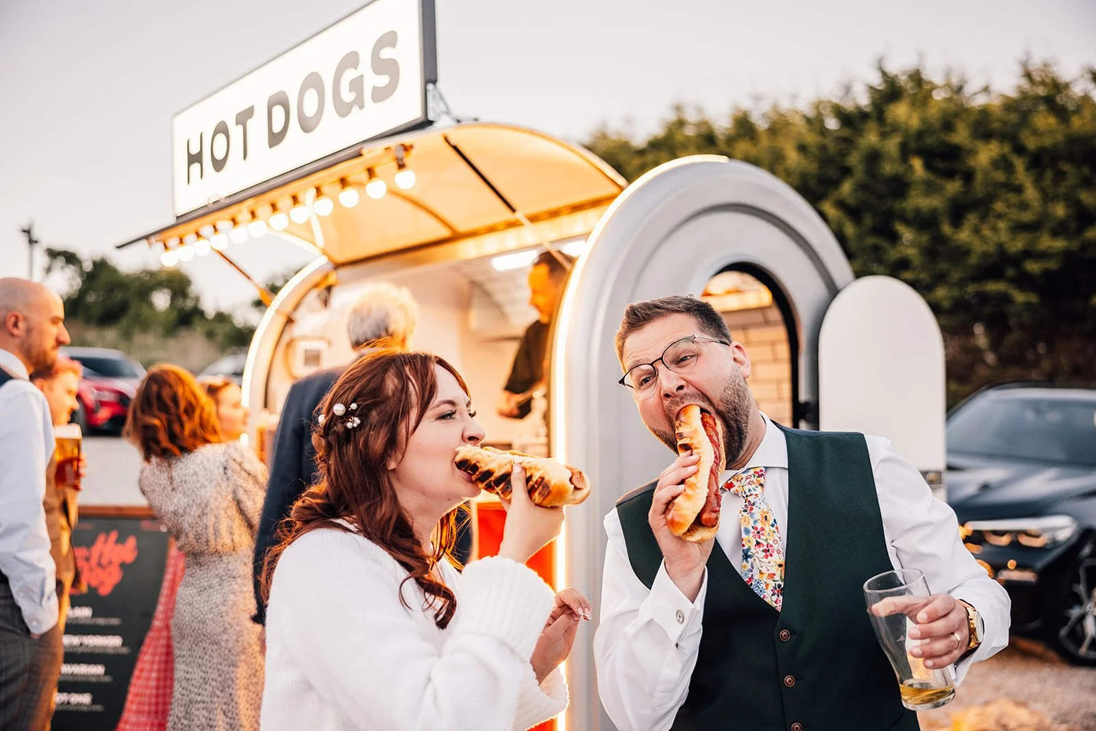 Bride and groom enjoying hot dogs at an evening wedding reception, served from a food truck, showcasing relaxed food truck hire for weddings