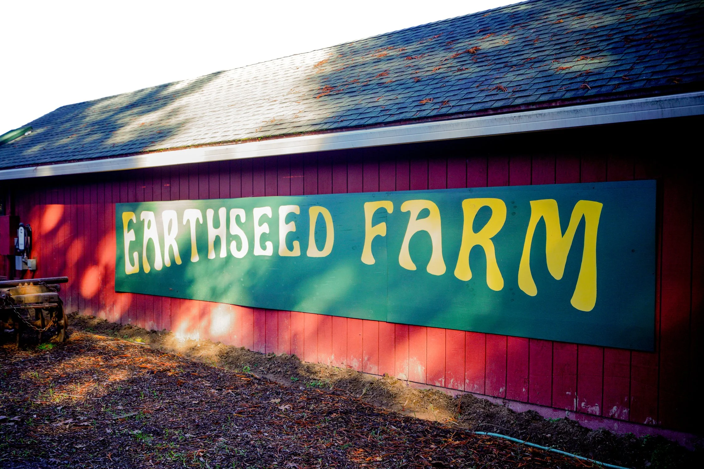 Large green wood panels with large curved yellow letters that read Earthseed Farm up against a red barn wall