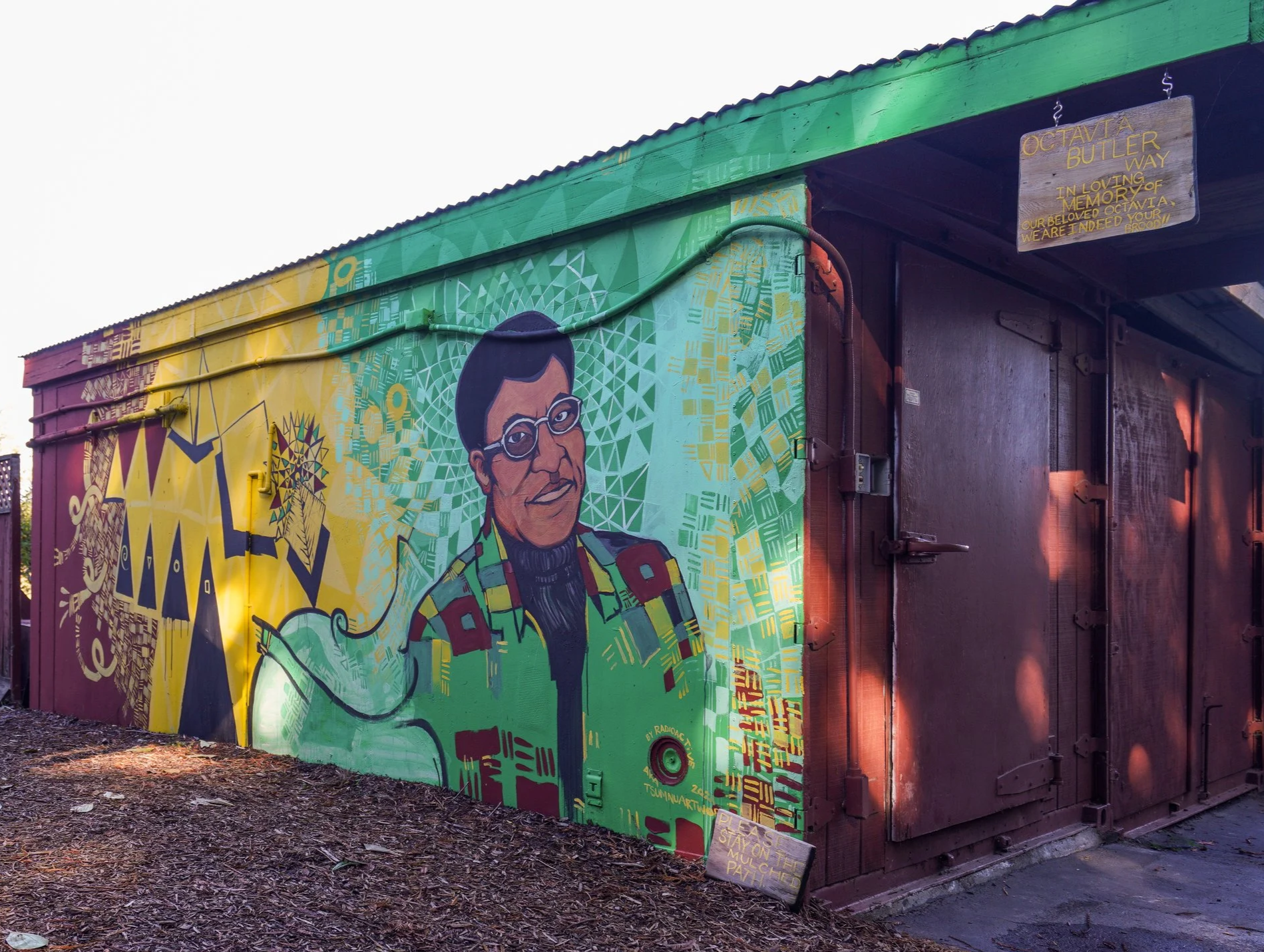 A mural of Octavia Butler mostly painted in different tones of green with accents of yellow, maroon and grey