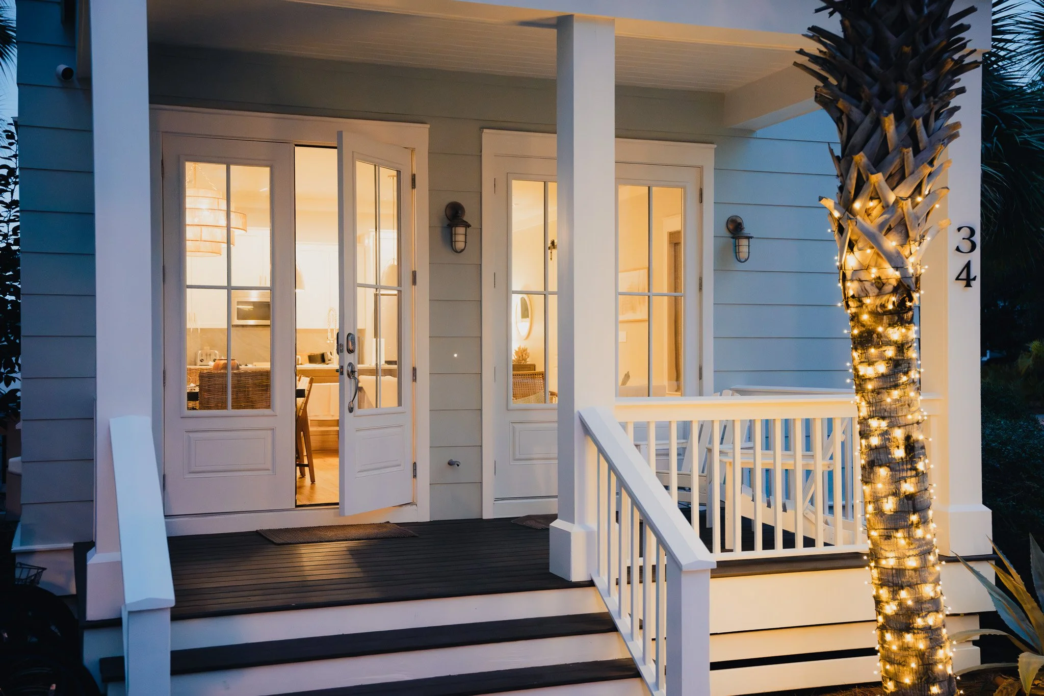 Front porch of a house with illuminated tree and open door revealing indoor lights.