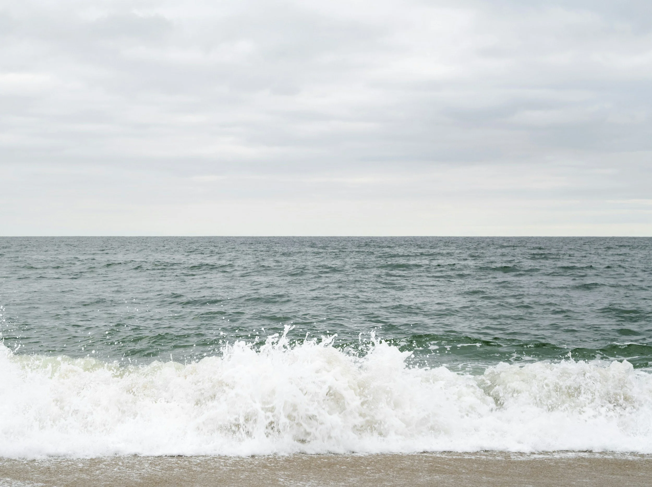 Ocean waves crashing on a sandy beach under an overcast sky.