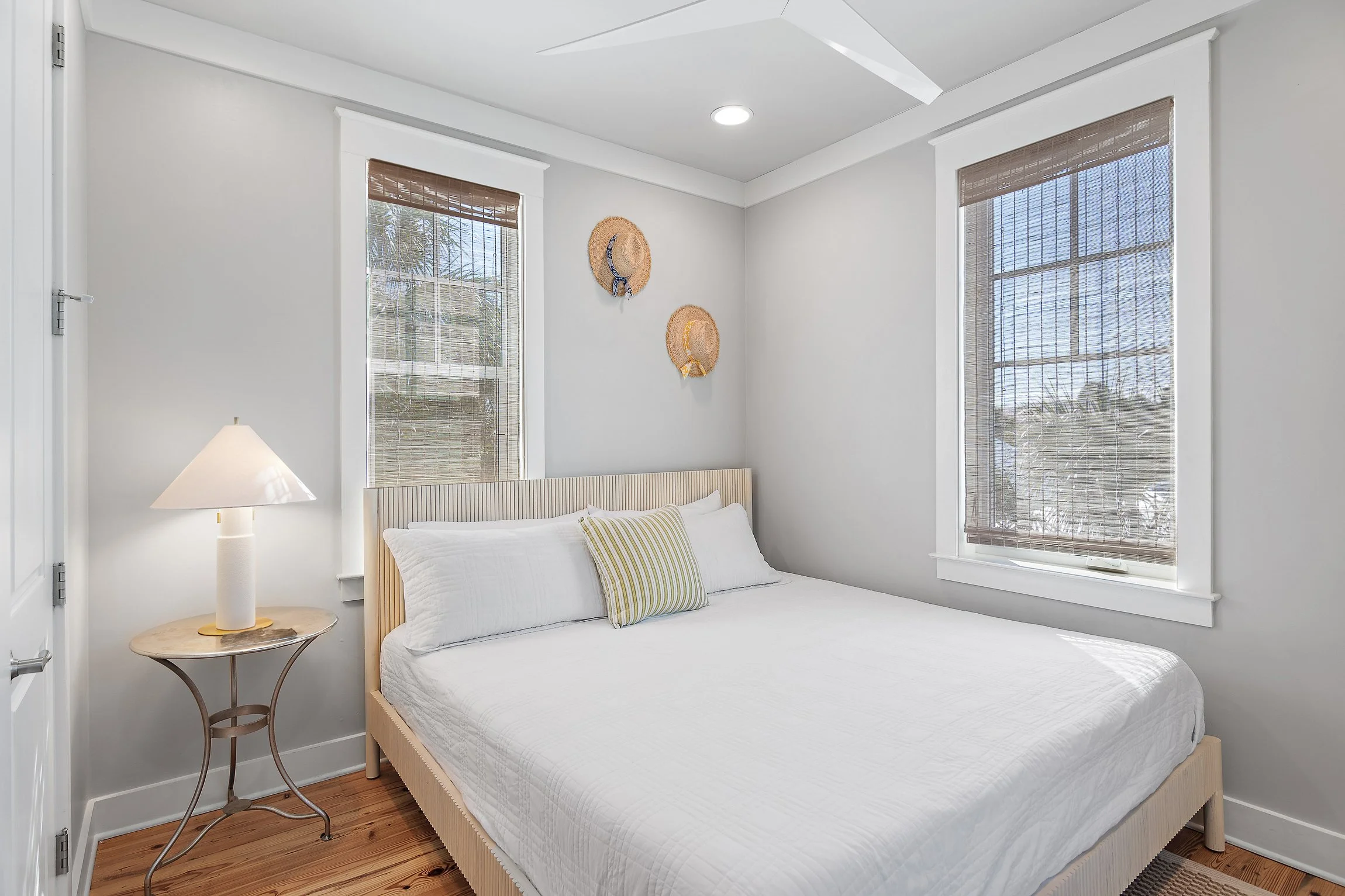 Bright and airy bedroom with a king-size bed and woven straw hats as wall decor. Large windows let in abundant natural light, creating a tranquil coastal retreat.