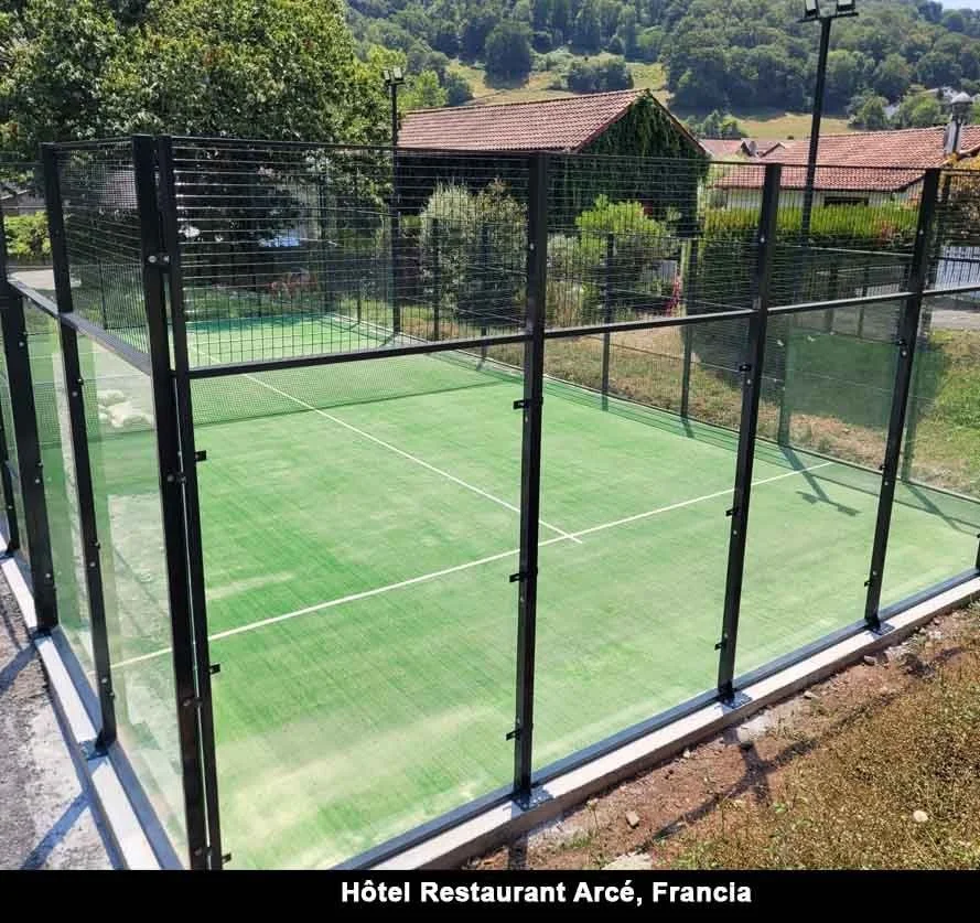 A glass-enclosed outdoor padel tennis court with a green playing surface, located at Hôtel Restaurant Arcé in France.