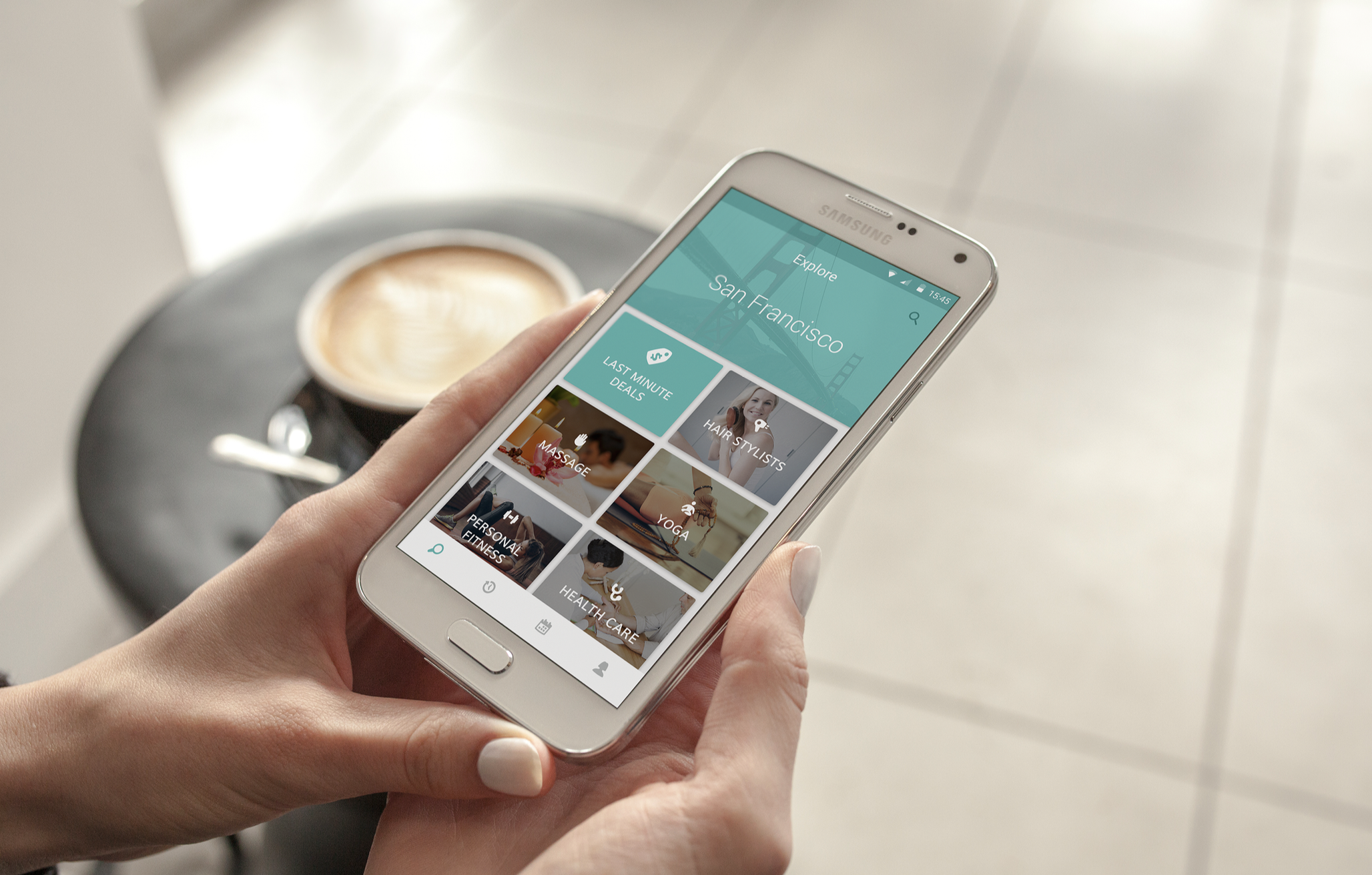 A person holding a smartphone displaying a San Francisco travel app with various activity options, including last-minute deals, massage, hair stylists, yoga, and personal fitness, with a coffee cup in the background.
