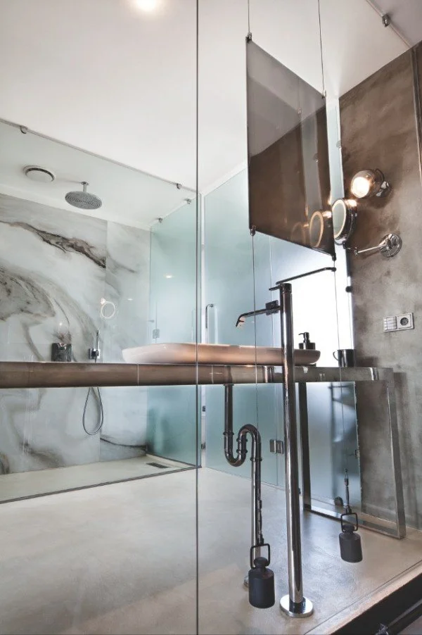 Modern bathroom with glass walls, marble bathtub, black fixtures, and a vessel sink on a concrete countertop.