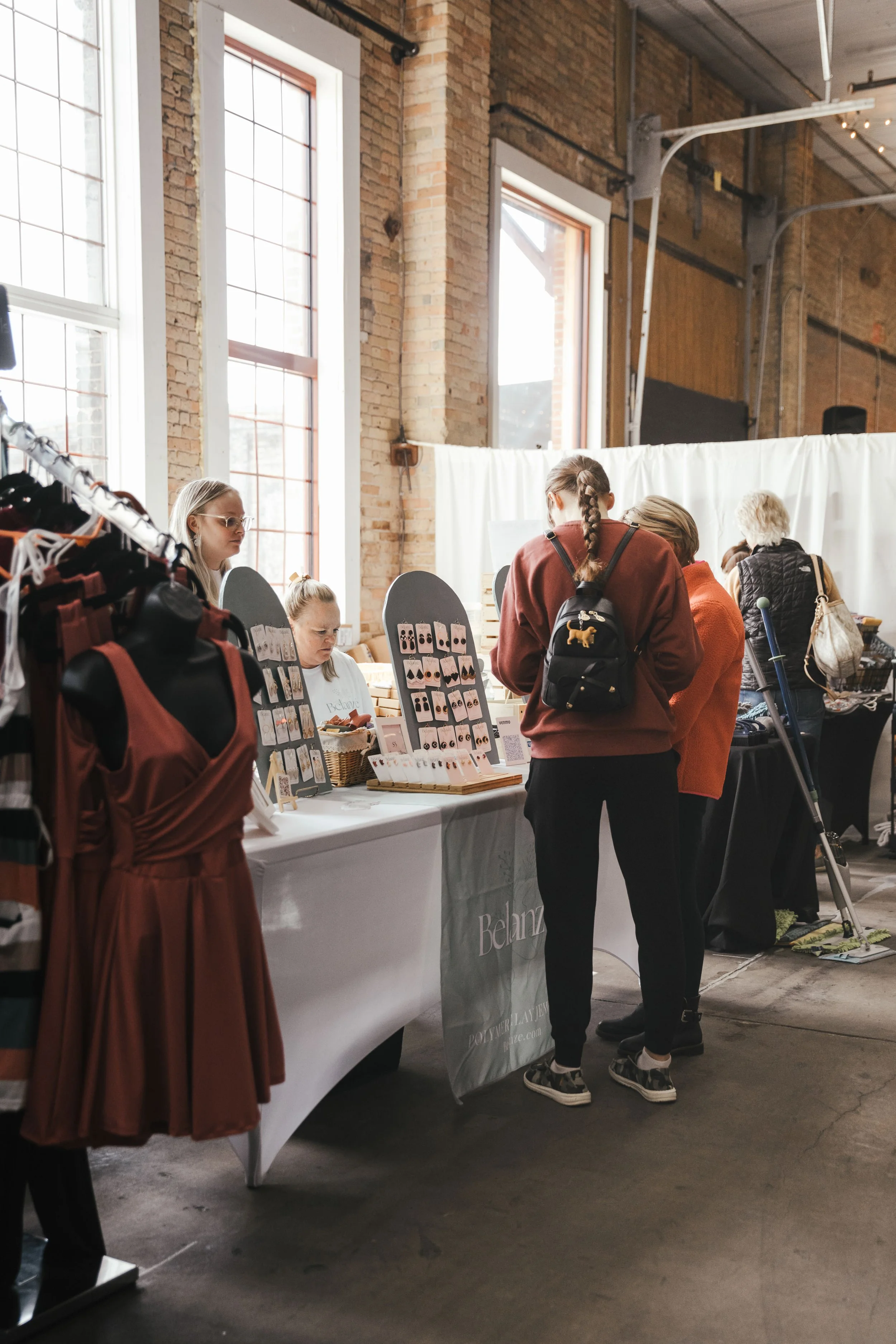 People shopping at a retail booth inside a brick-walled venue with high windows and industrial ceilings.