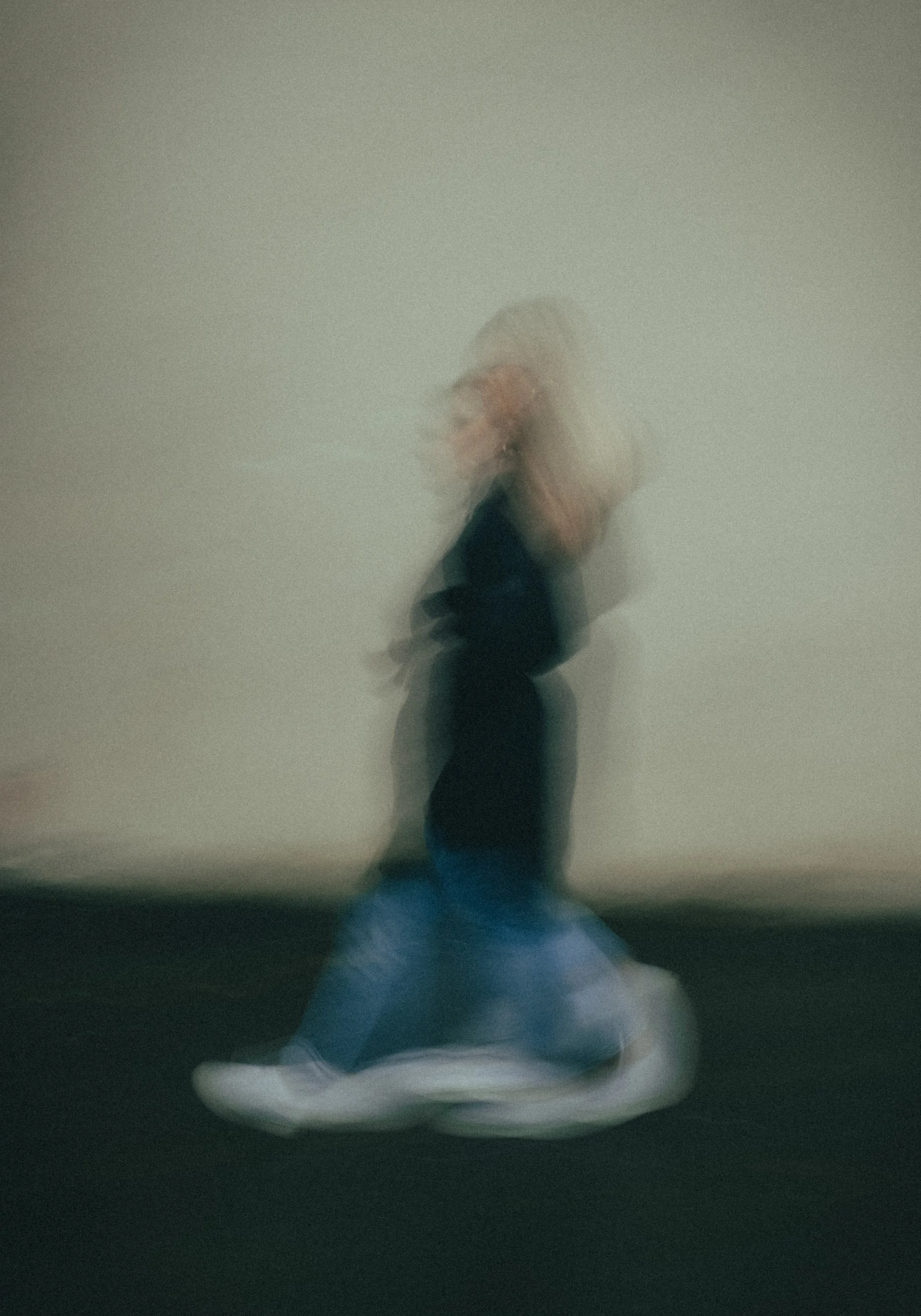 Et bilde av en person som går, med bevegelsesuskarphet, mot en nøytral vegg. Personen har blondt hår og er iført svarte klær og blå jeans.