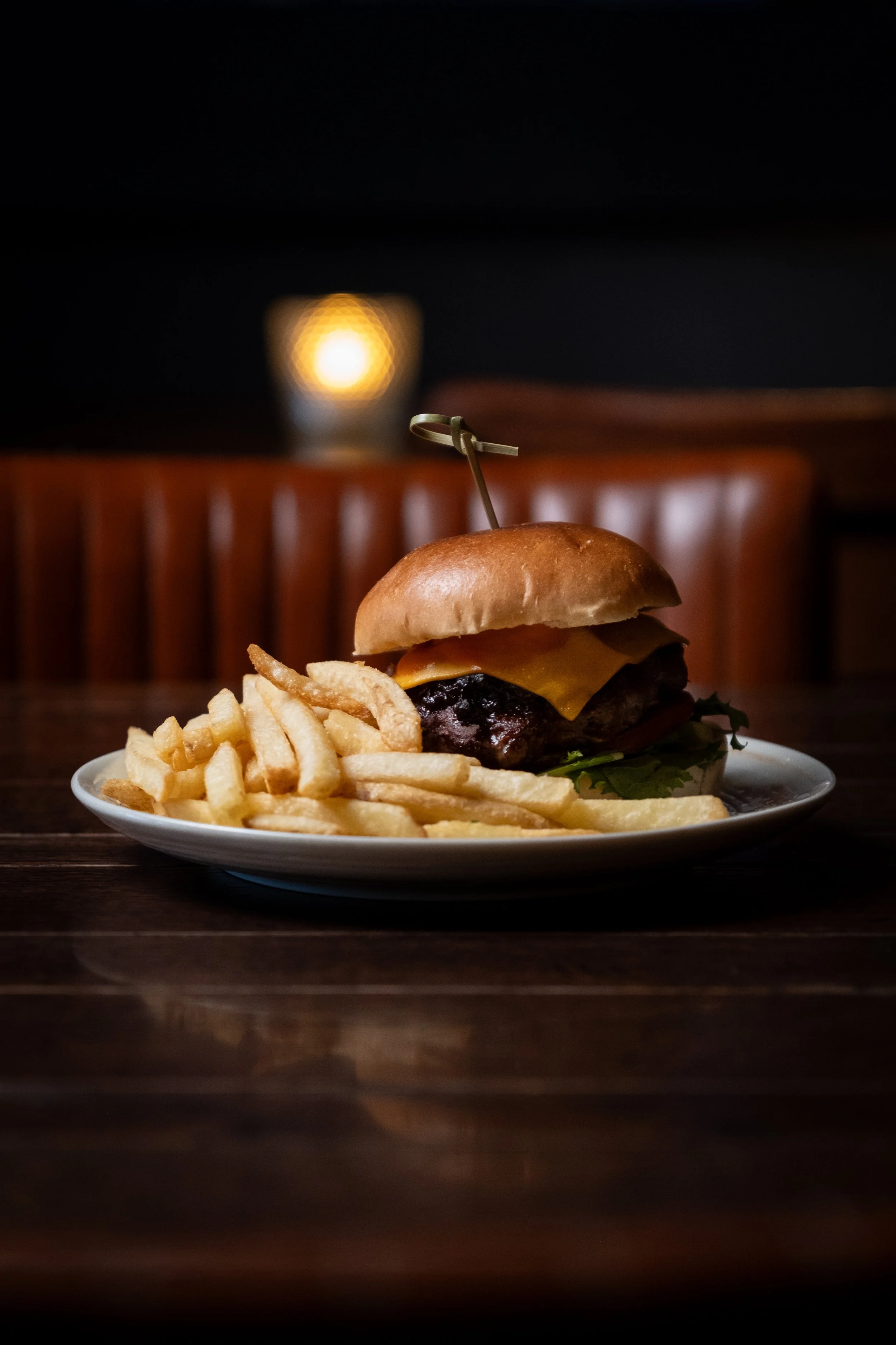 Hamburger med ost, salat, og pommes frites på en hvit tallerken, plassert på en mørk trebord.