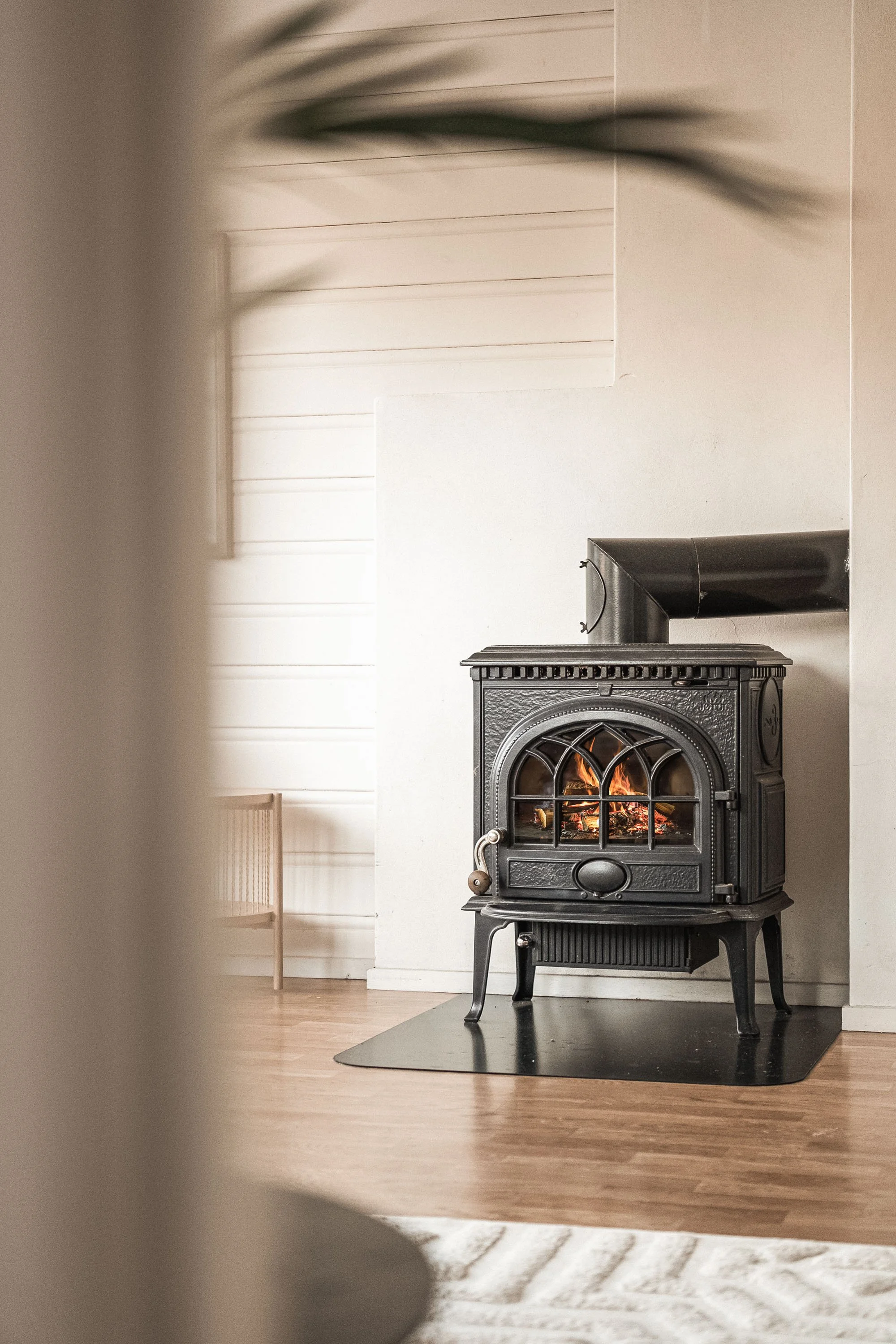En svart kamin med brennende ild i et lyst rom med tregulv og hvite vegger.