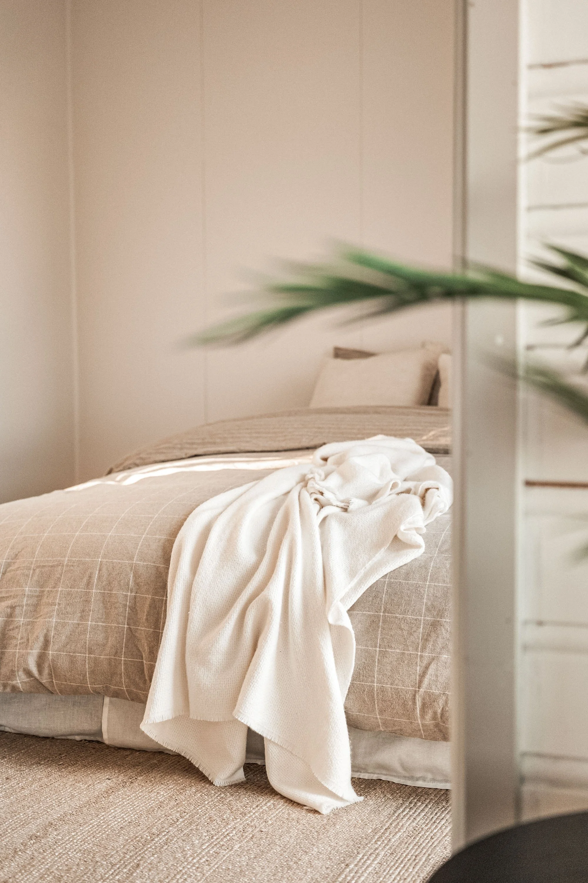 Seng med beige- og hvitrutete sengetøy, hvit genser og puter i bakgrunnen på rommet.