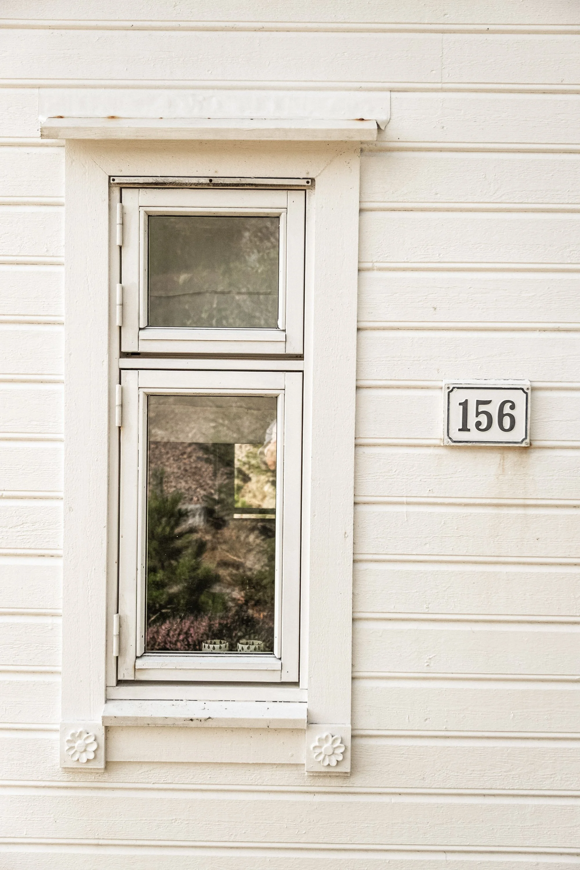 Nærbilde av et hvitt vindu på en trebebygning med husnummer 156.