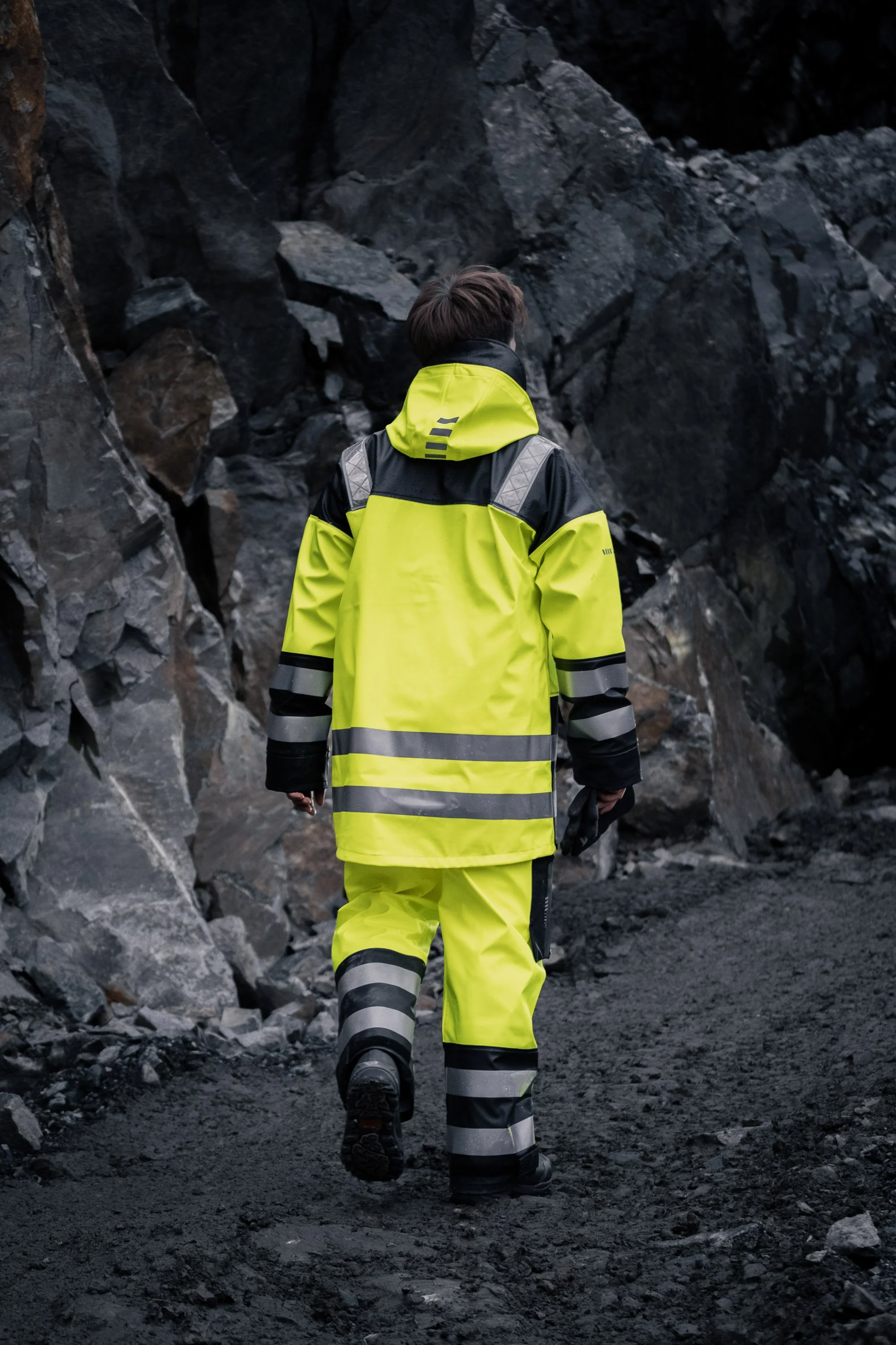 En person iført høyt synlig refleksjakke og jakt, som går gjennom en steinete, mørk dal