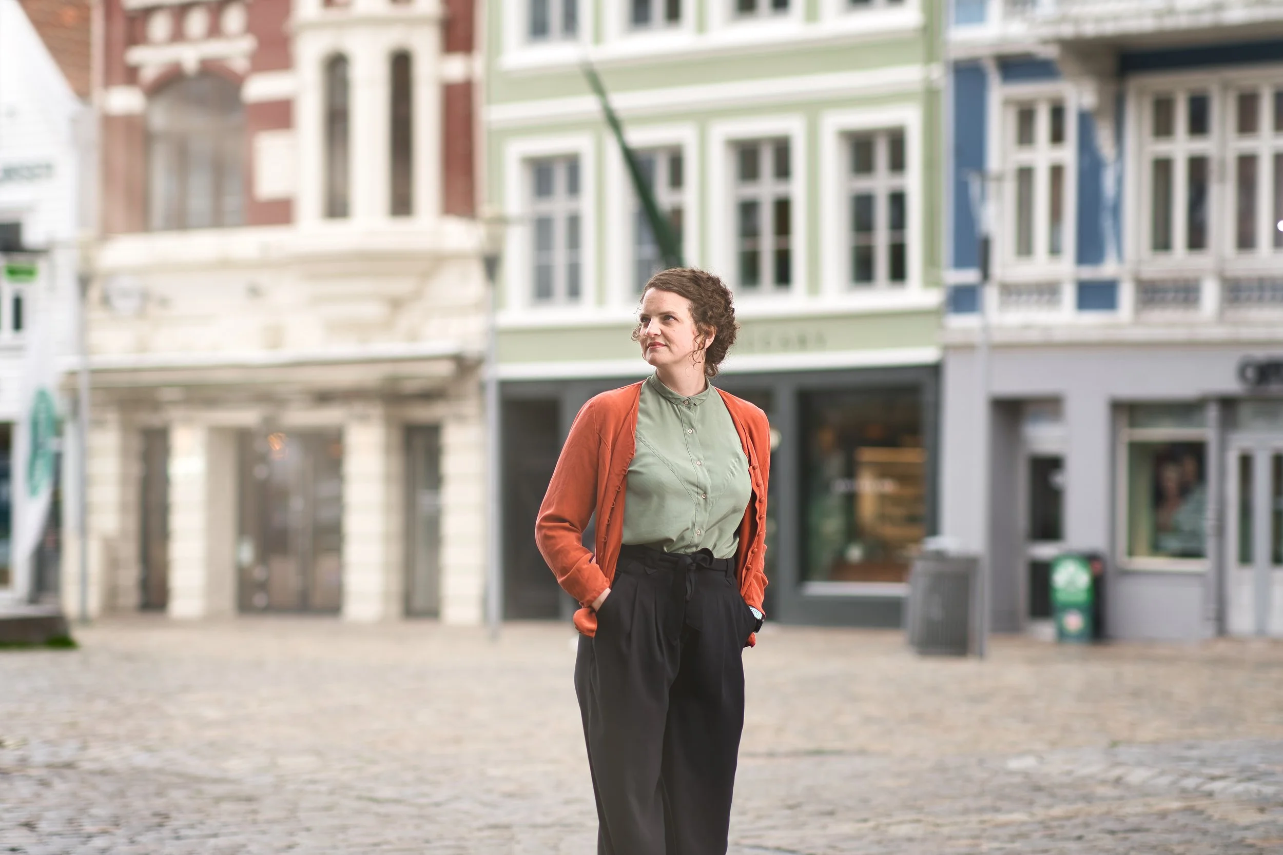 En kvinne står på en brosteinbelagt gate med fargerike bygg i bakgrunnen.