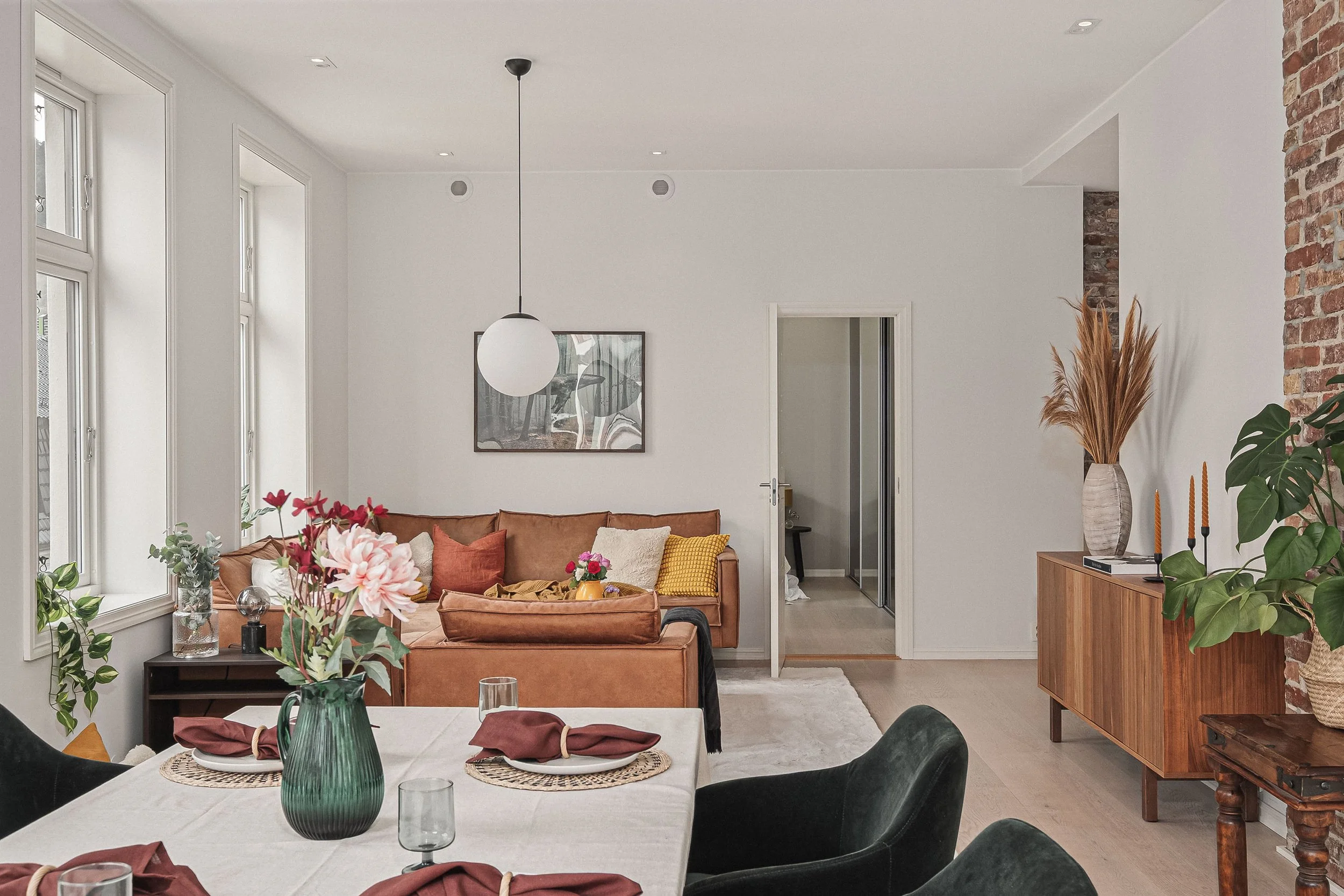 Innendørs stue med en rund spisekrok og sofa, små planter, en malt vegg, og en åpen dør mot et annet rom.