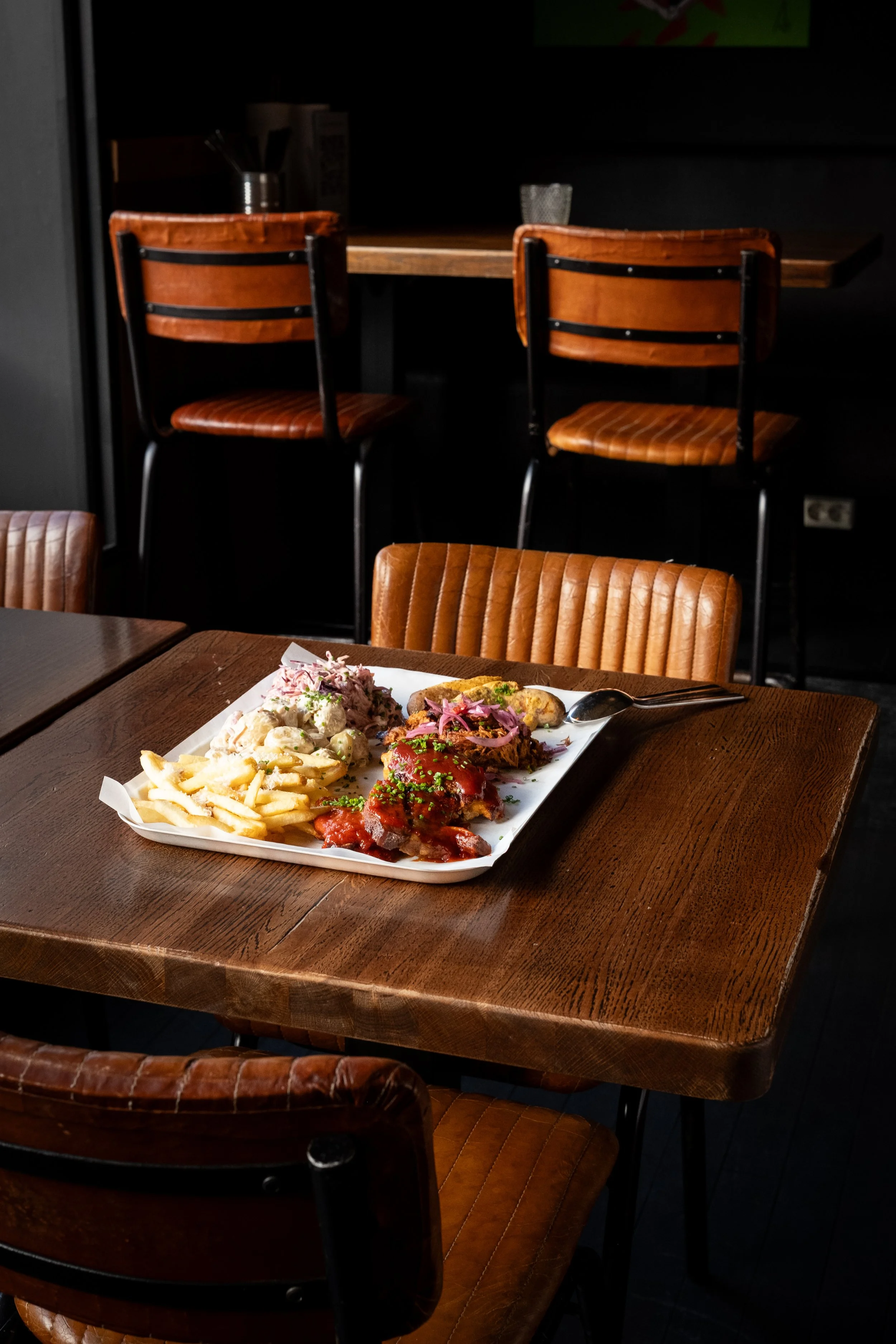 En tallerken med mat på et trebord i en restaurant, omgitt av brune lærstoler og høye stolar i bakgrunnen.