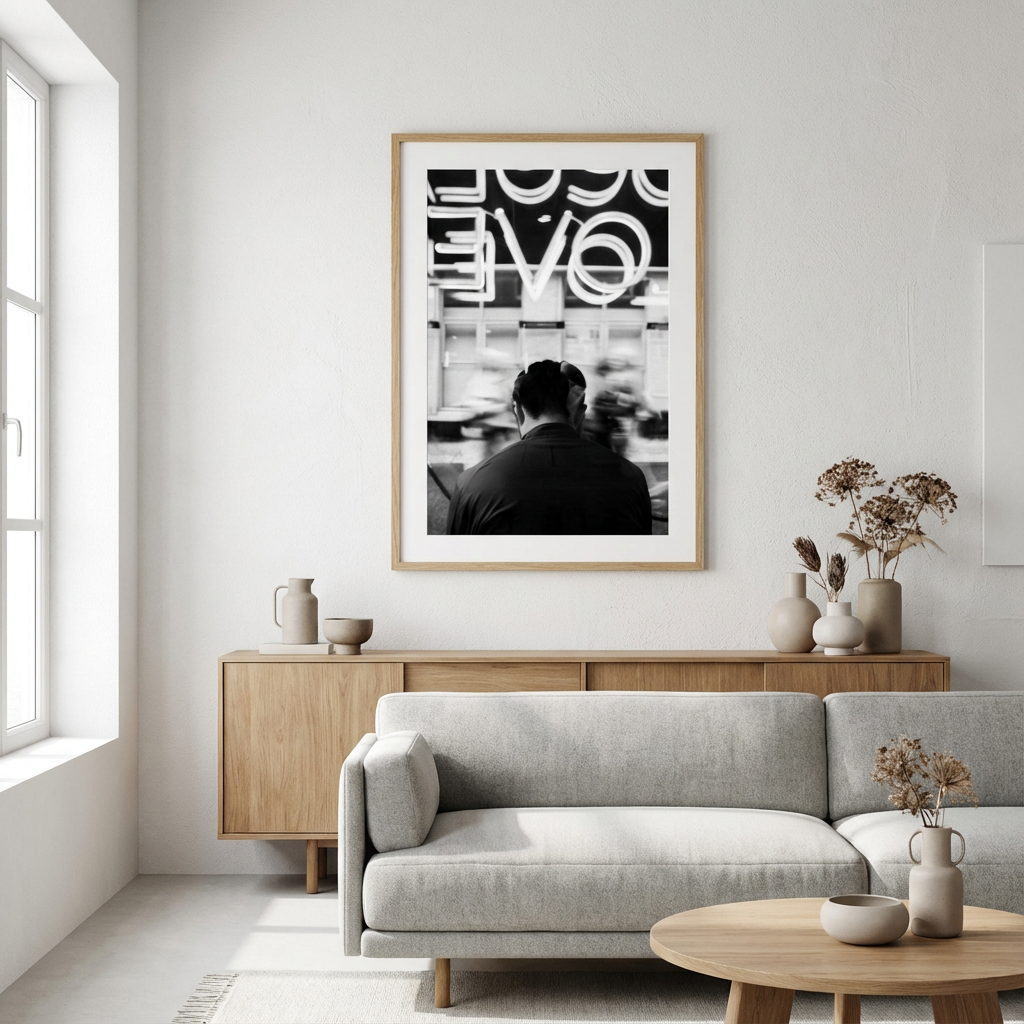 Et moderne stueinnredning med en lys grå sofa, en rundt trebord, og en sidebord med flere hvite og beige vaser med tørkede blomster. Et svart-hvitt bilde av en person på en bygate henger på veggen bak sofaen.