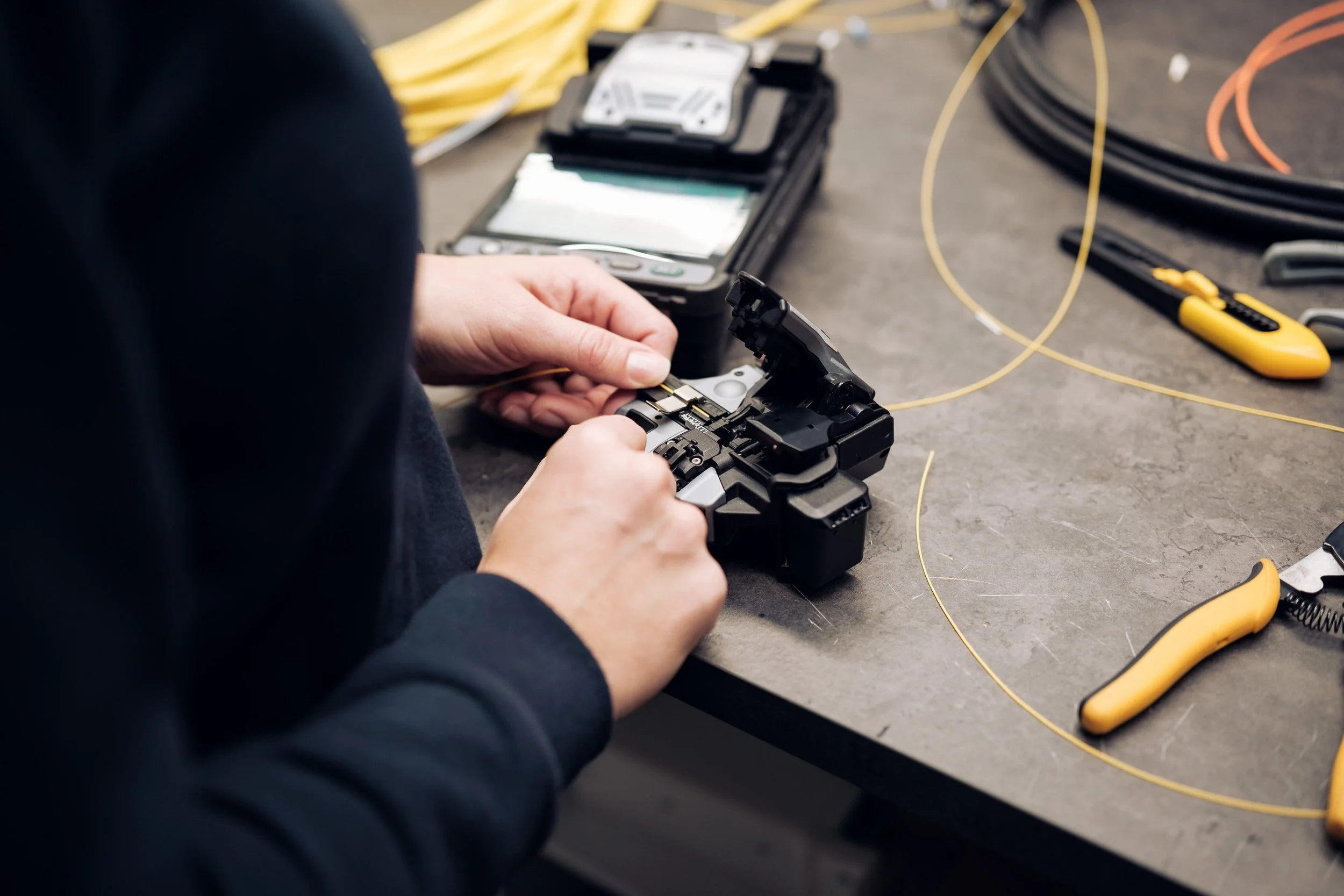 En person reparerer en elektronisk enhet på et verkstedbord med verktøy og utstyr rundt seg.
