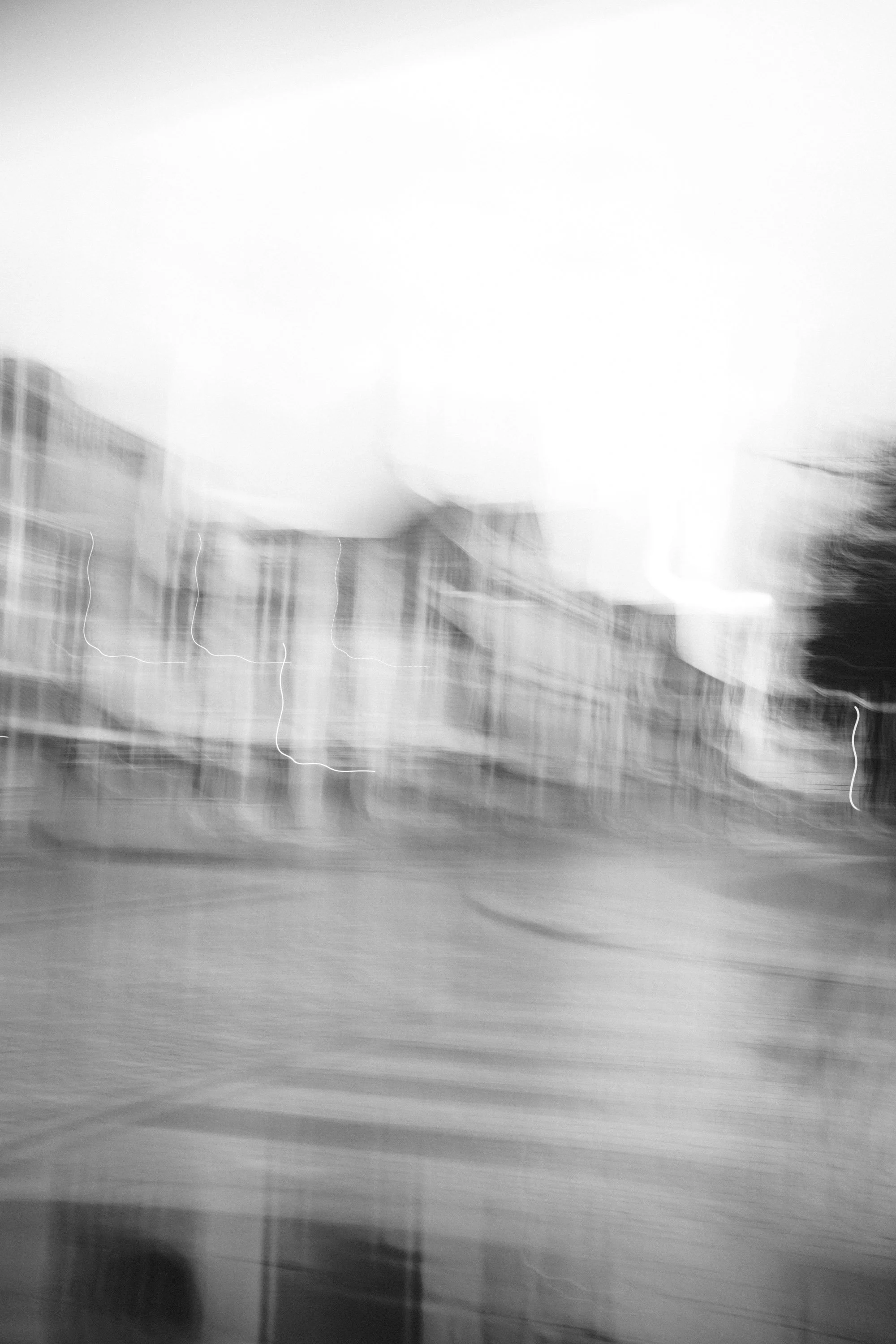 Sort-hvitt bilde av en uskarp bygate med bygninger og trær.