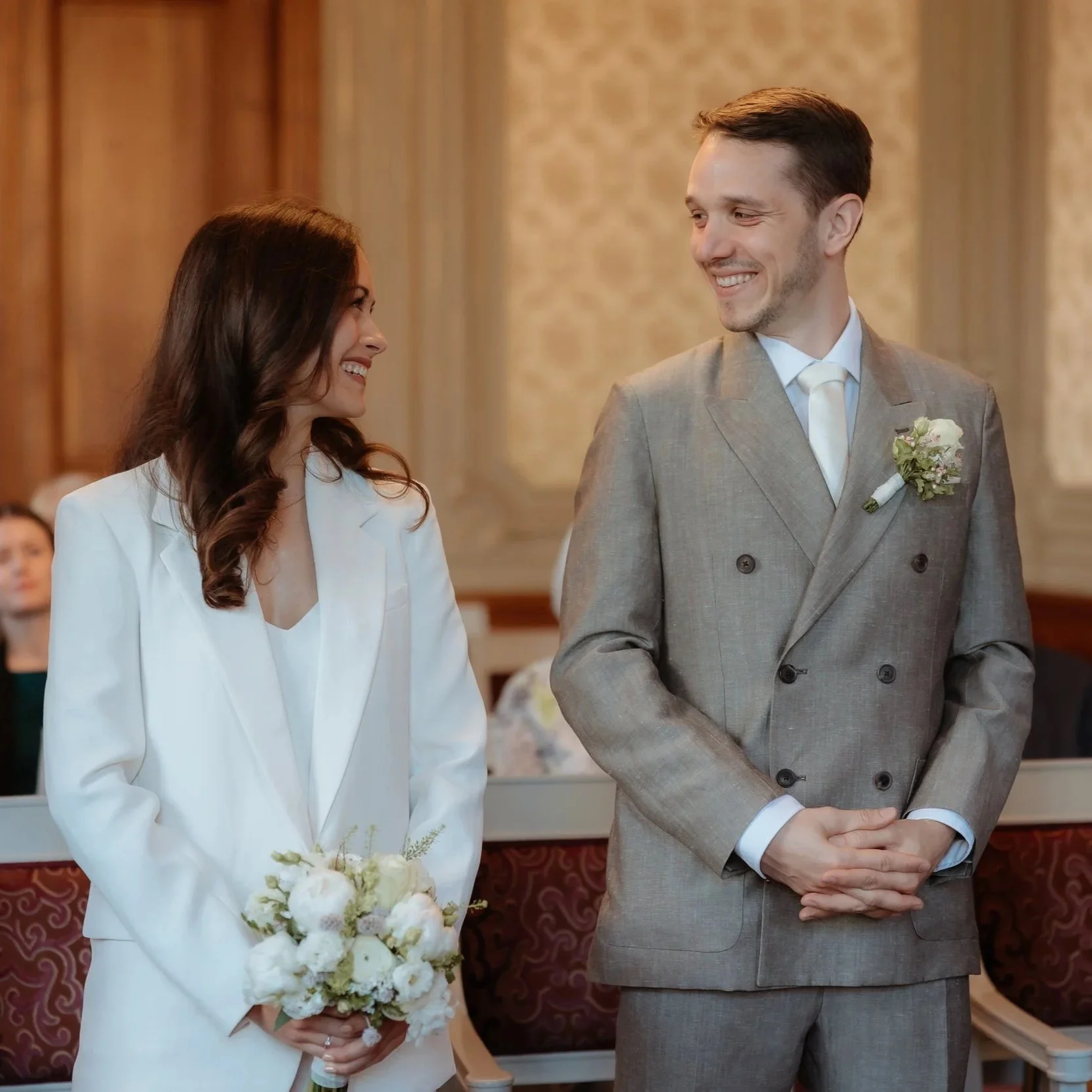 Hochzeitspaar zeigt Eheringe vor versammelter Gesellschaft in festlichem Saal.