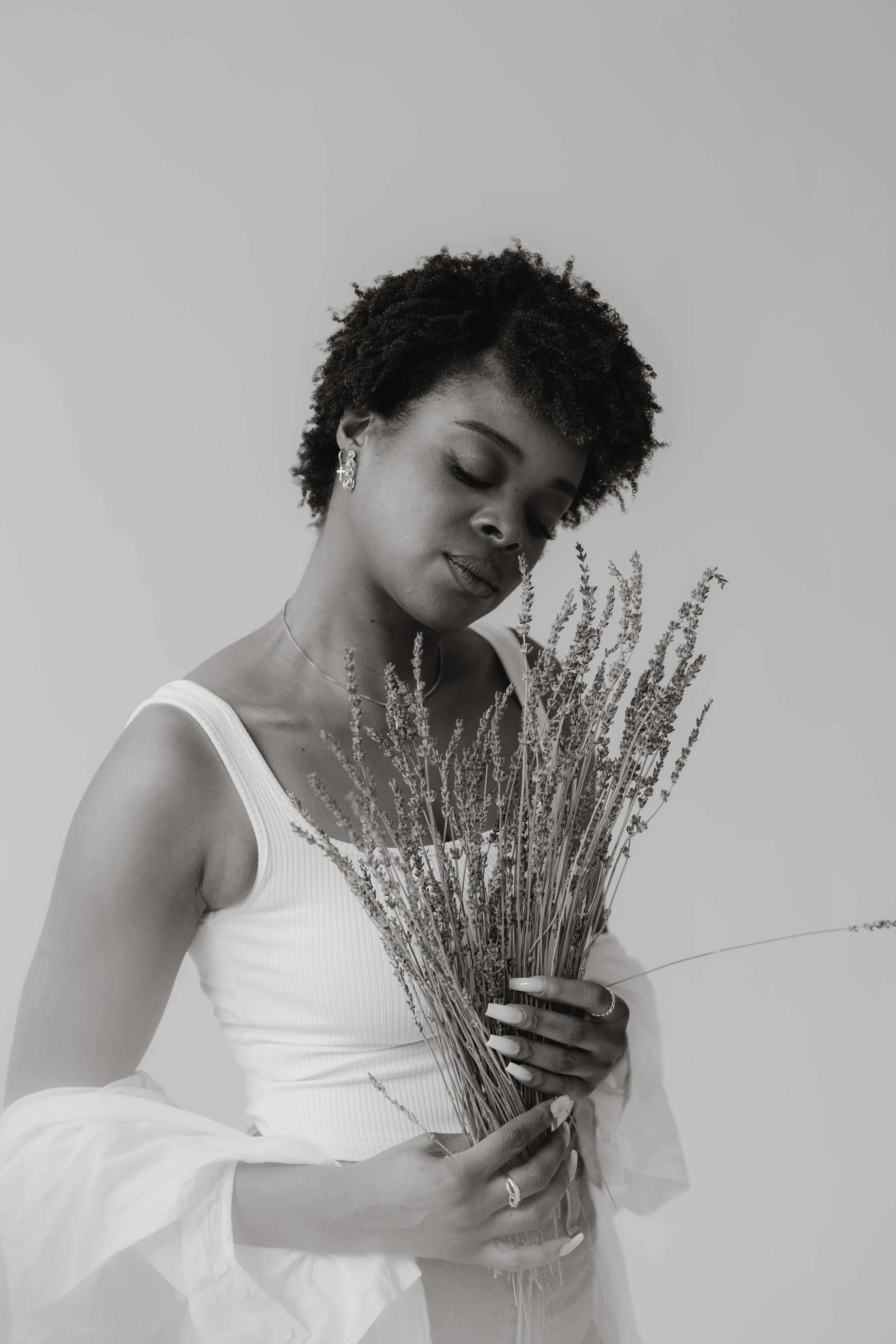 Schwarz-weiß-Foto einer Frau mit kurzen, lockigen Haaren, die einen Strauß Trockenpflanzen hält.