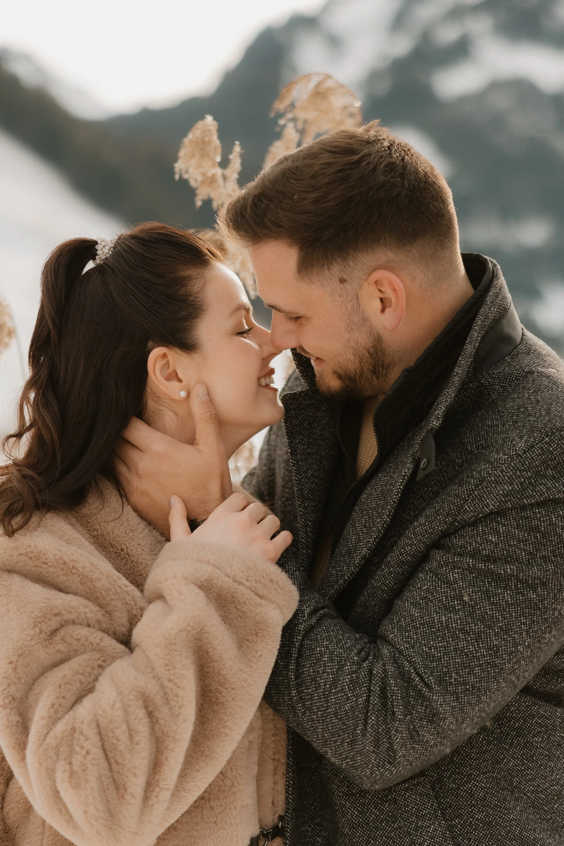 Ein Paar ist eng umarmt, ihre Stirnen berühren sich, in einer Winterlandschaft mit Berg im Hintergrund.