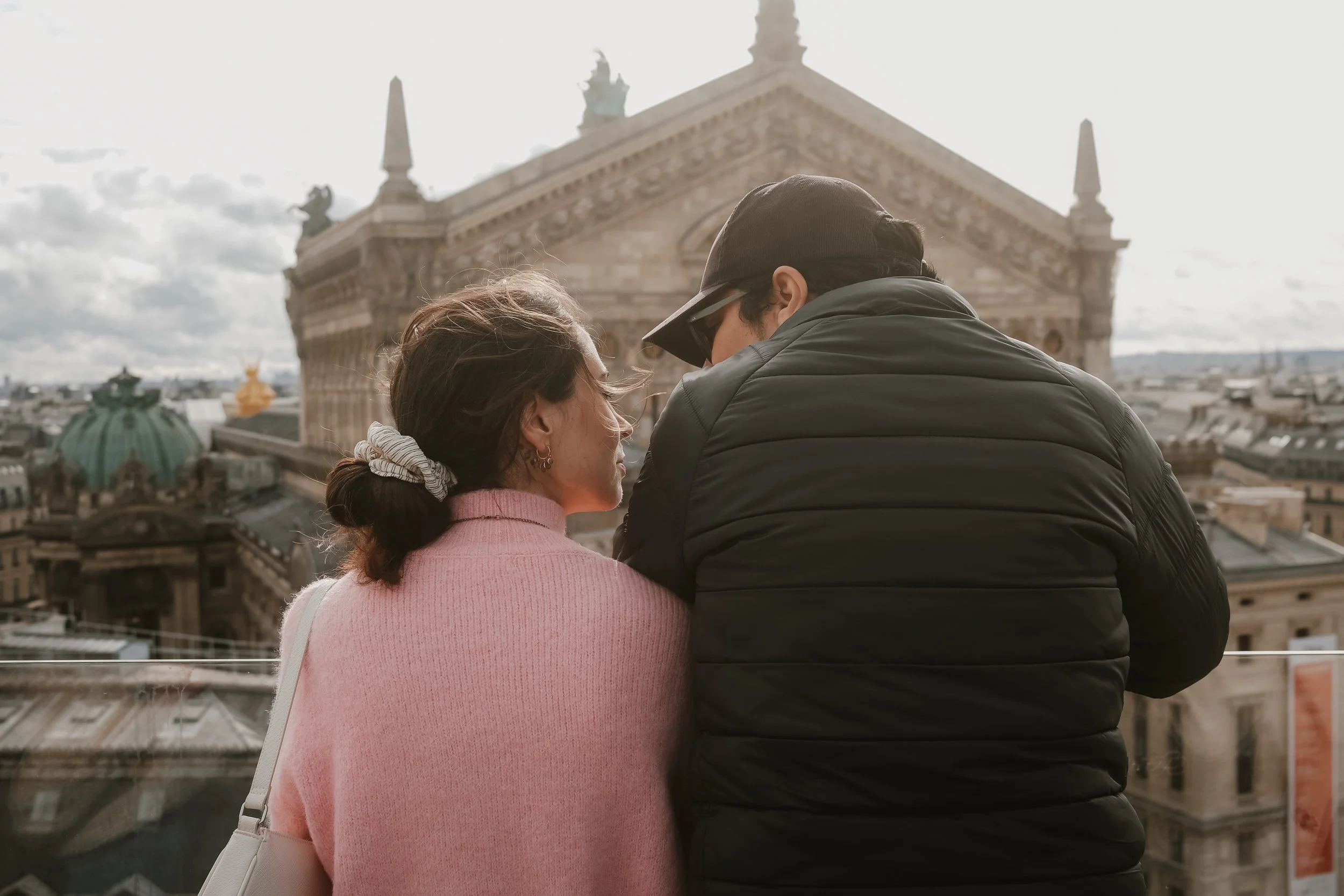 Paar, das auf einer Dachterrasse in einer Stadt steht, blickt auf historische Gebäude in der Ferne