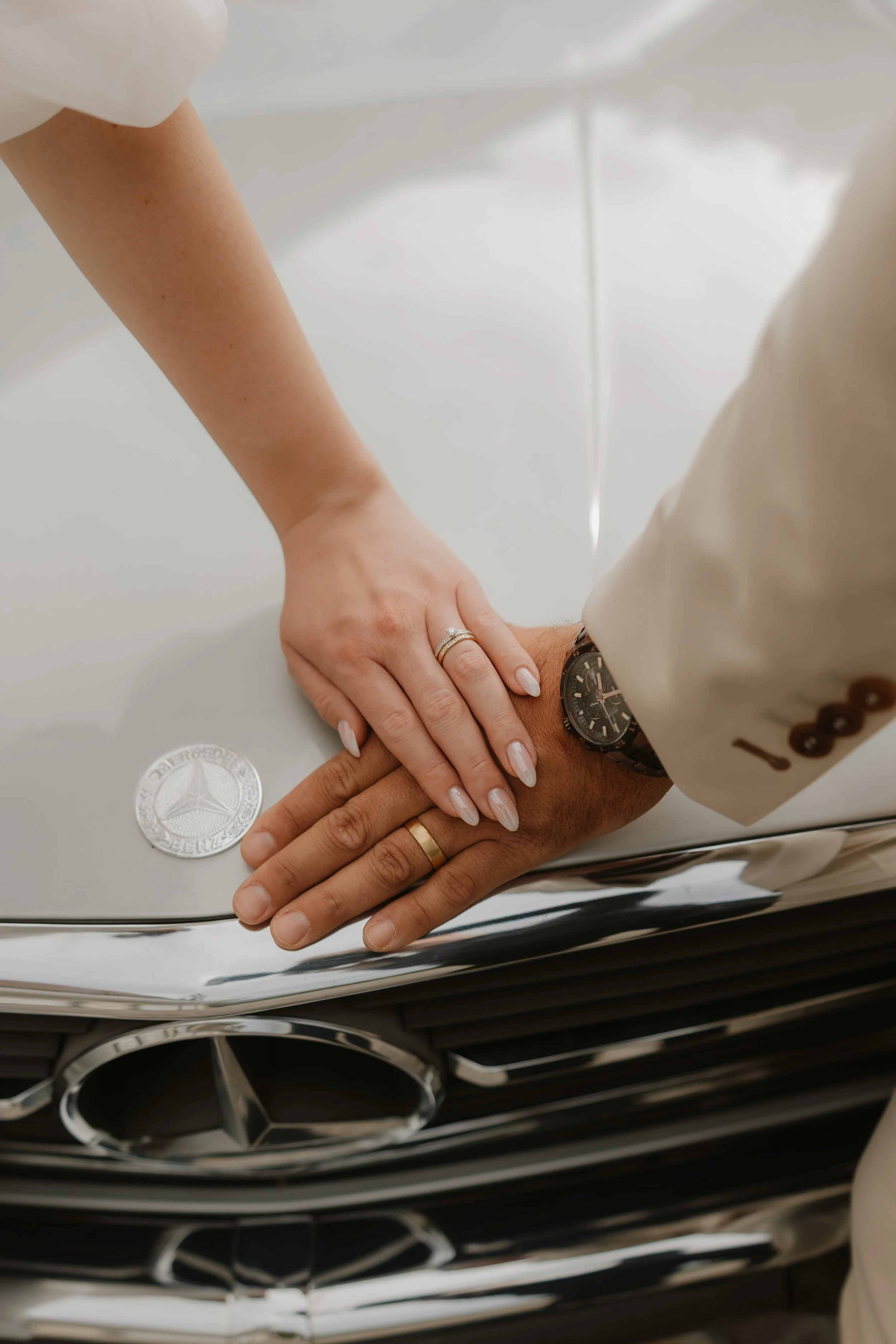 Zwei Hände, die auf den Grill eines Mercedes-Fahrzeugs legen, mit einem Mercedes-Emblem im Vordergrund.
